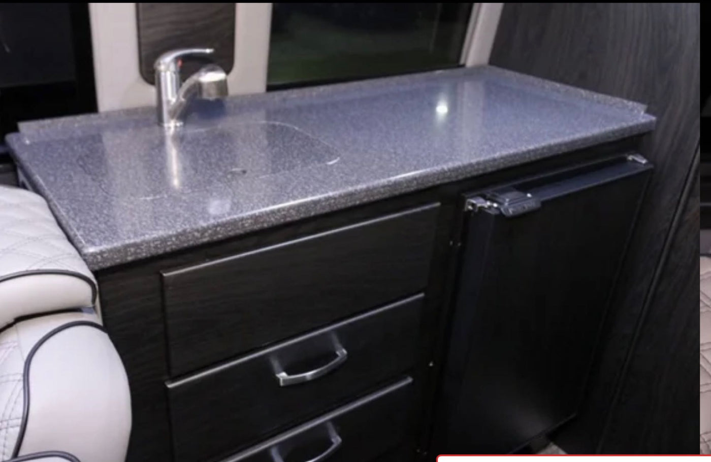 RV rental kitchenette featuring a speckled countertop, sink, under-counter storage drawers, and a compact refrigerator. — photo 14