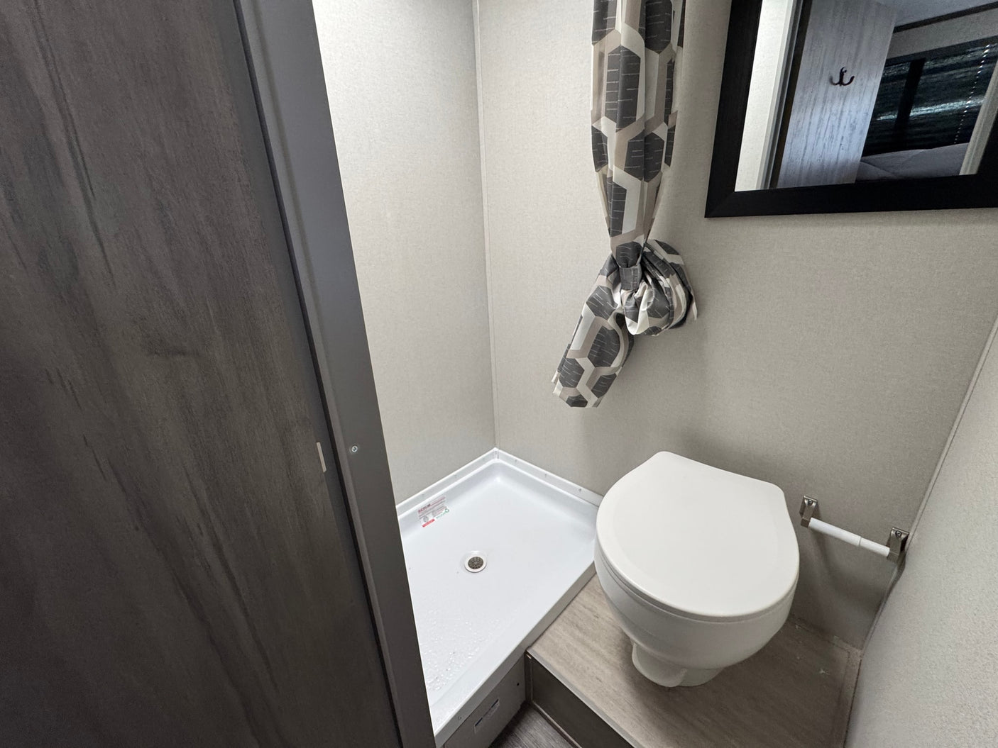 RV rental's compact bathroom showing a white shower stall, toilet, and tied-back geometric shower curtain.