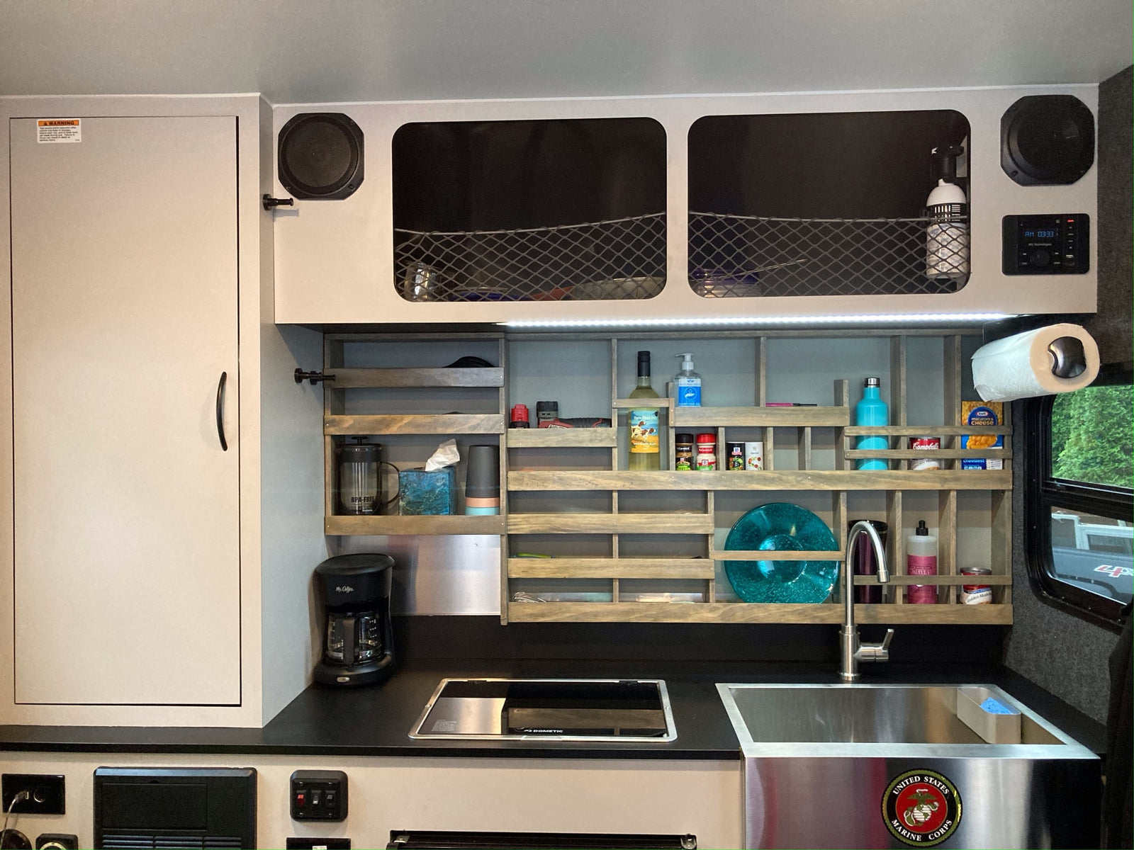Compact RV rental kitchen featuring a Dometic cooktop, sink, coffee maker, and smart shelving with essentials for travel.