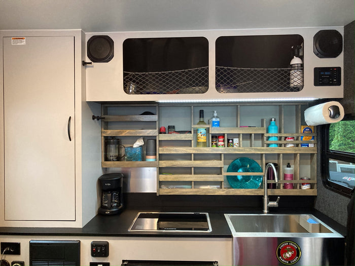 Compact RV rental kitchen featuring a Dometic cooktop, sink, coffee maker, and smart shelving with essentials for travel.