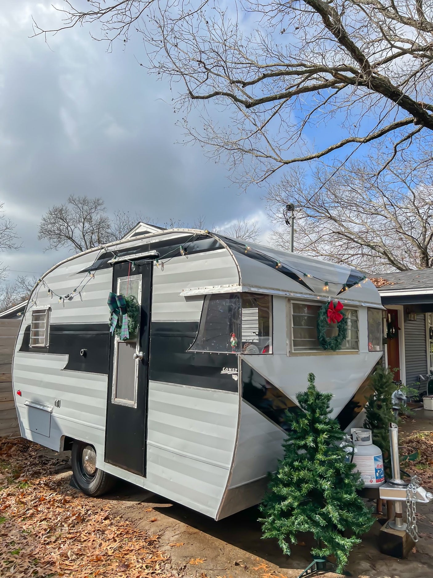 Charming vintage Comet travel trailer, adorned with holiday decor & string lights. Ideal RV rental for festive adventures!