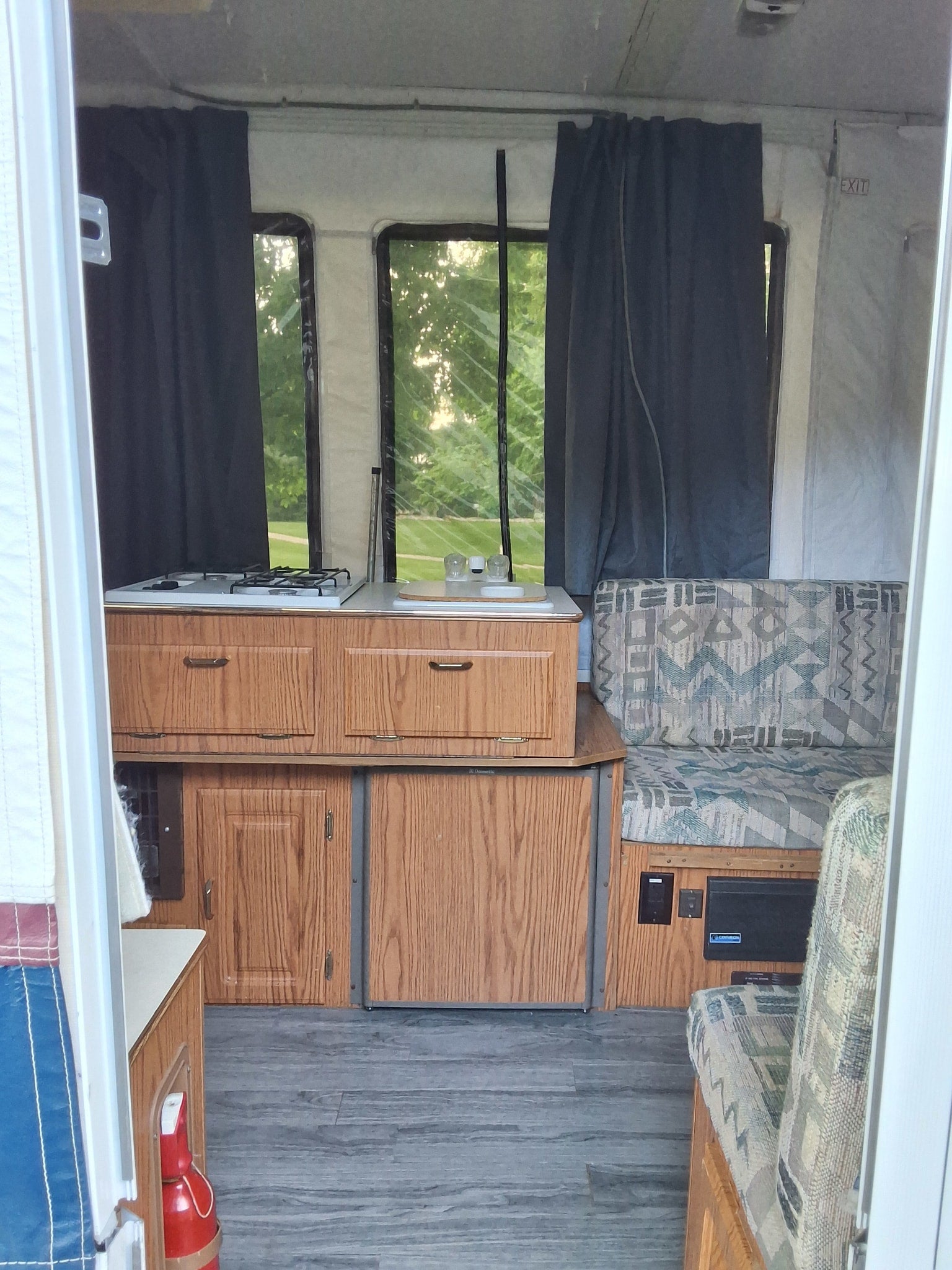 Inside this practical RV rental: a neat kitchen area with stove, sink, compact fridge, and cozy patterned seating for your adventures.