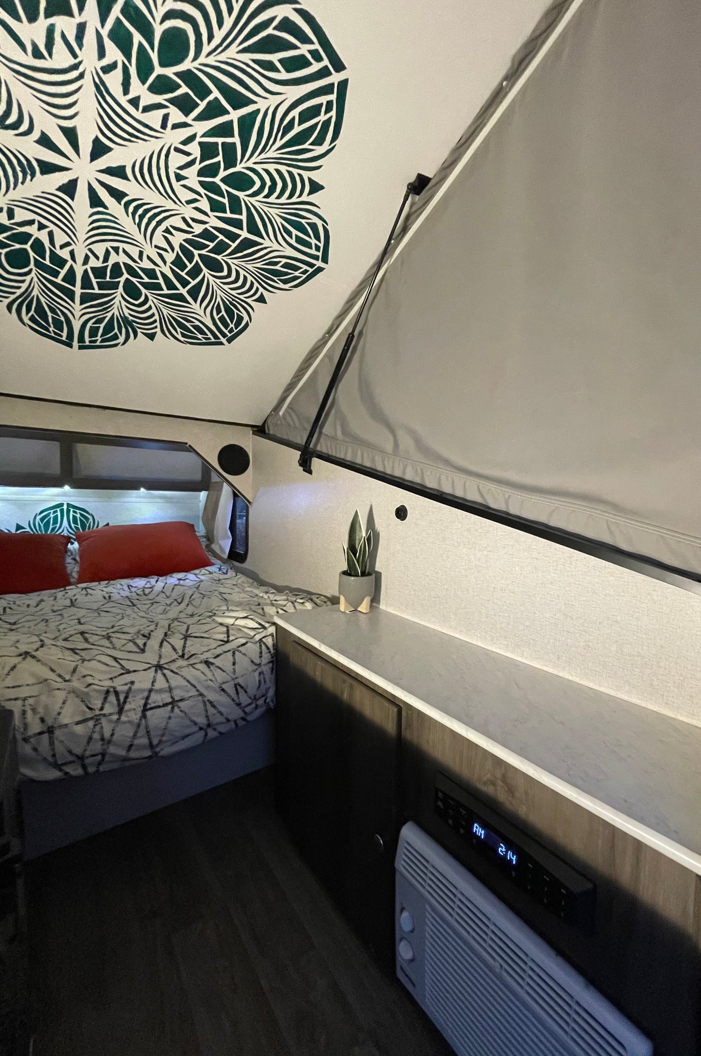 Cozy RV rental interior featuring a bed with patterned bedding, a decorative mandala on the ceiling, and a heater next to a digital clock.