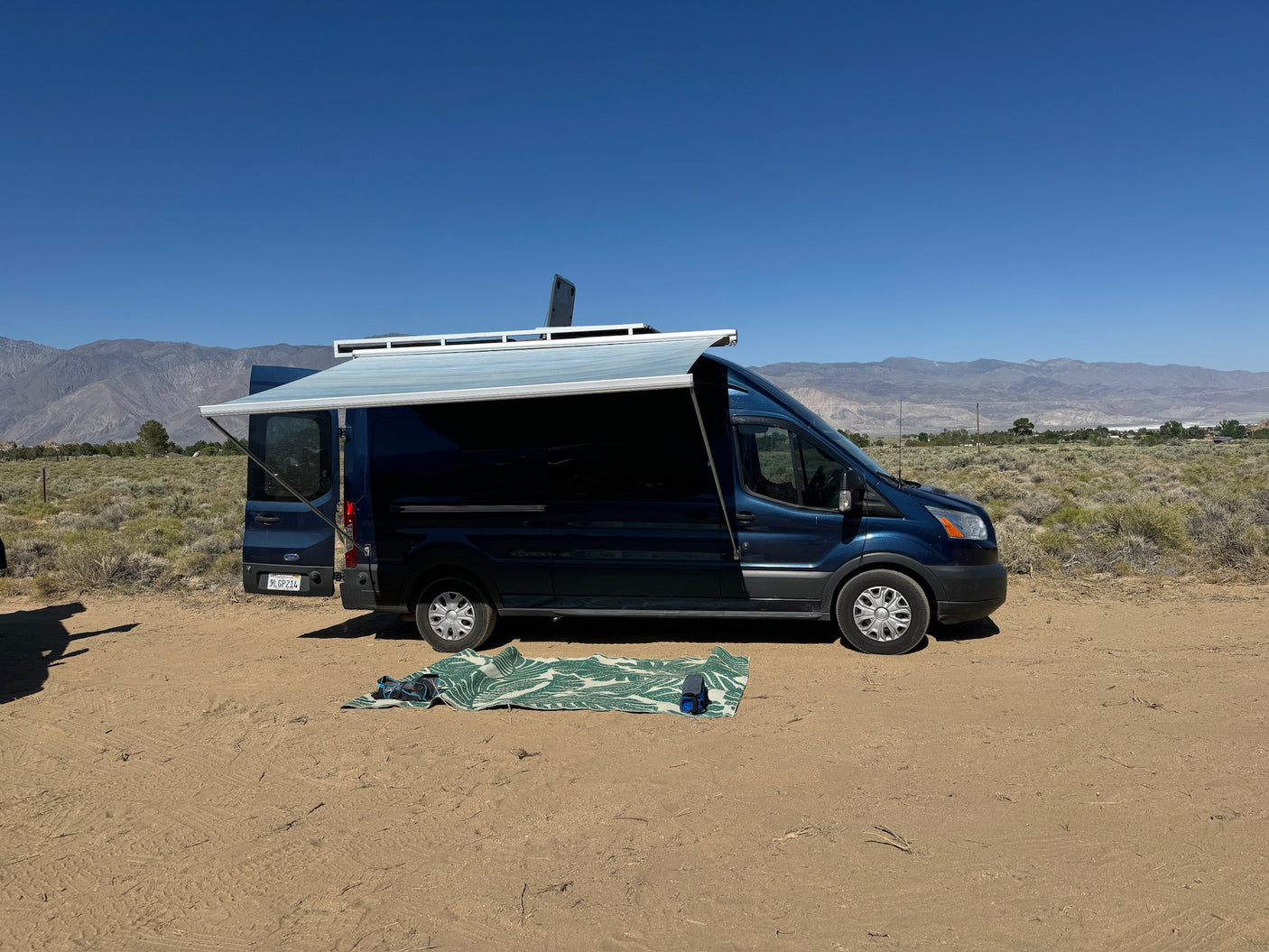 Blue Ford Transit van, an ideal RV rental with awning deployed for van life camping in a scenic desert.