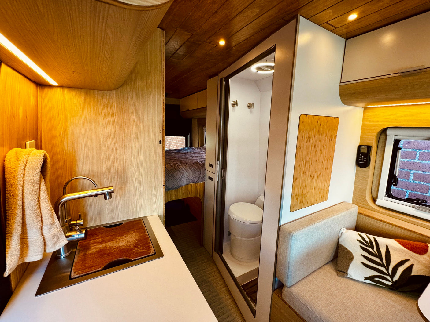 Modern rv rental interior featuring a compact kitchen, bathroom with toilet, cozy seating, and a bed in the background.