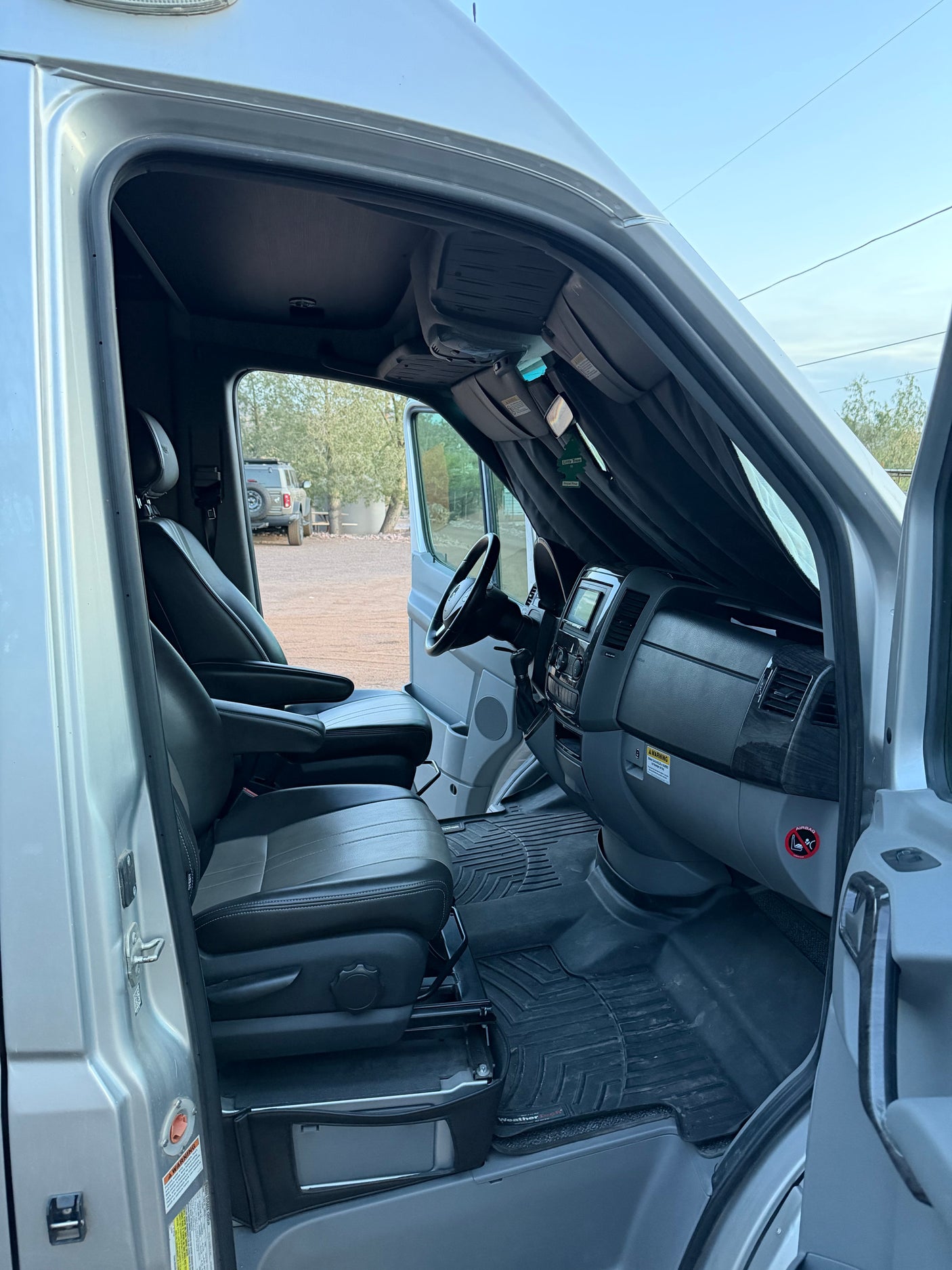 Spacious rv rental cab with black leather seats, dashboard, and steering wheel, viewed from the open driver's door.