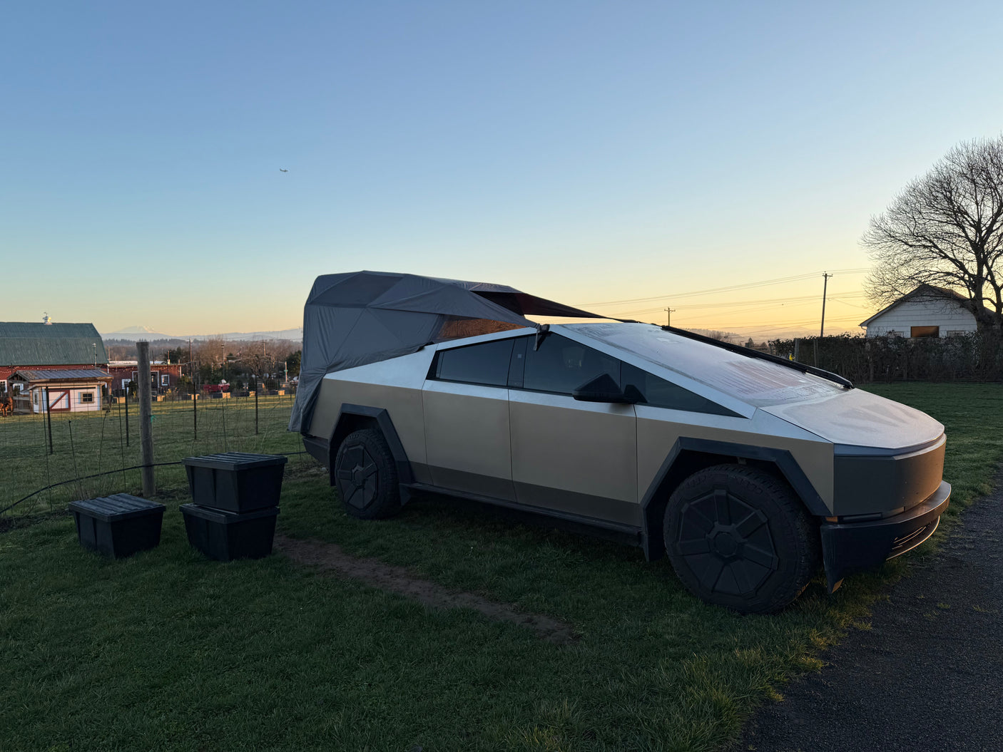 A Tesla Cybertruck with a unique tent/camper attachment, set in a rural landscape, hints at an innovative rv rental.