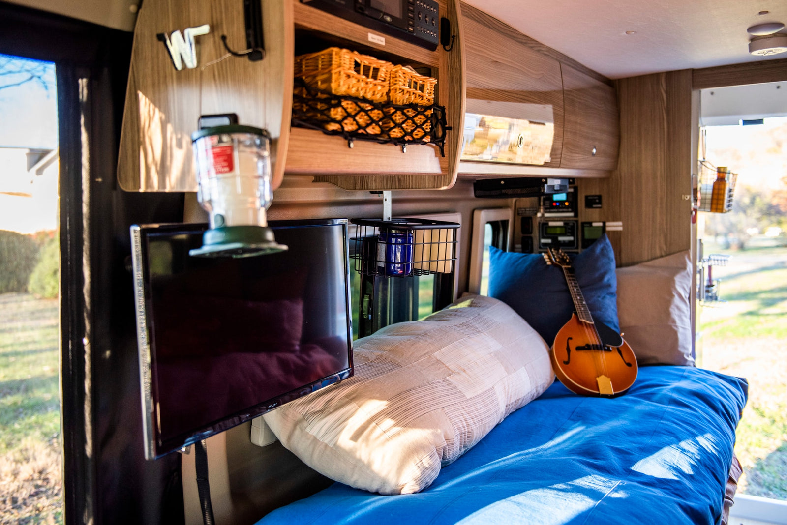 Inside a modern **rv rental**: a comfy bed, wall-mounted TV, musical mandolin, and clever storage.