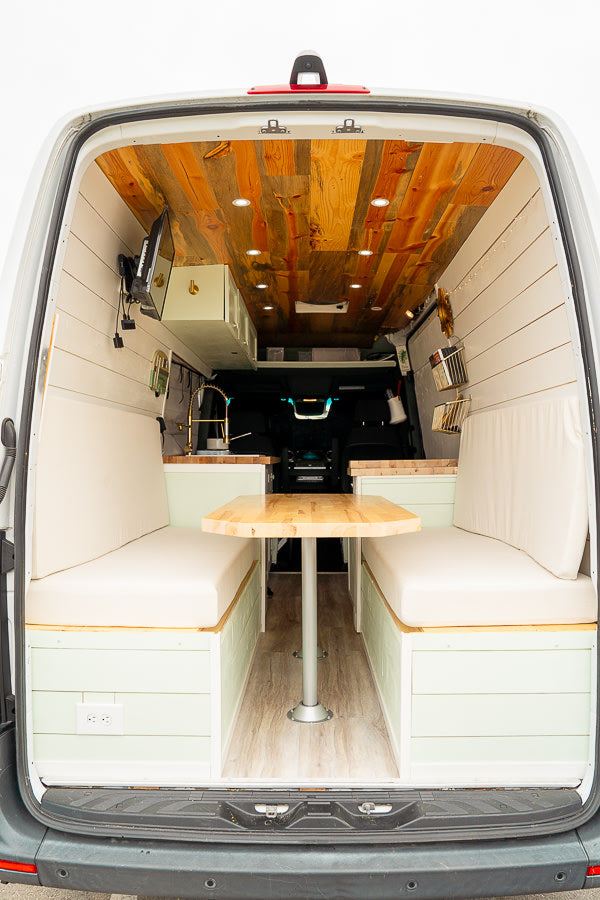 Stylish **RV rental** van conversion interior showing a cozy dining area, wood ceiling, and compact kitchen setup.