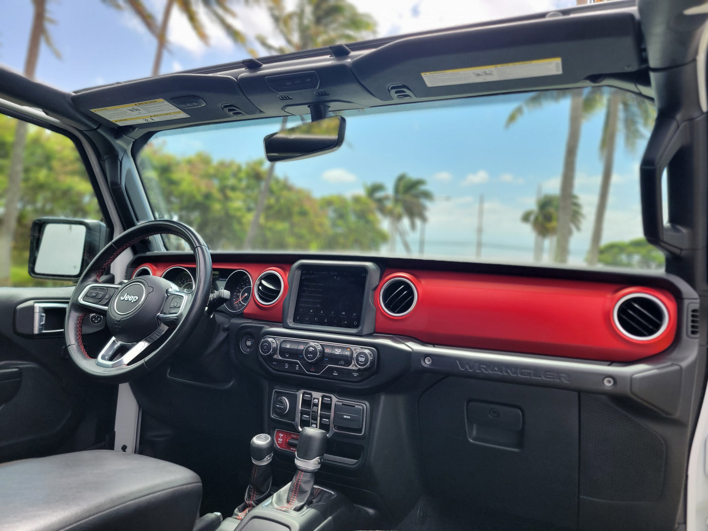 Jeep Wrangler RV rental interior with a vibrant red dash, open roof, & tropical views. Your adventure vehicle awaits!