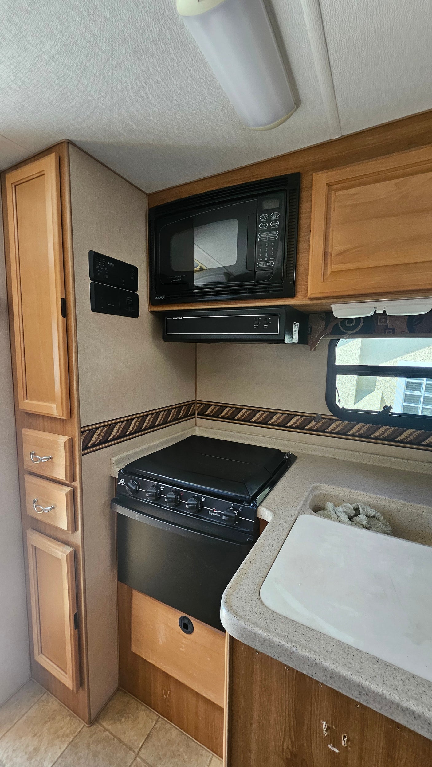 This clean RV rental kitchen features a microwave, stove, sink, and wood cabinetry, perfect for on-the-go cooking.