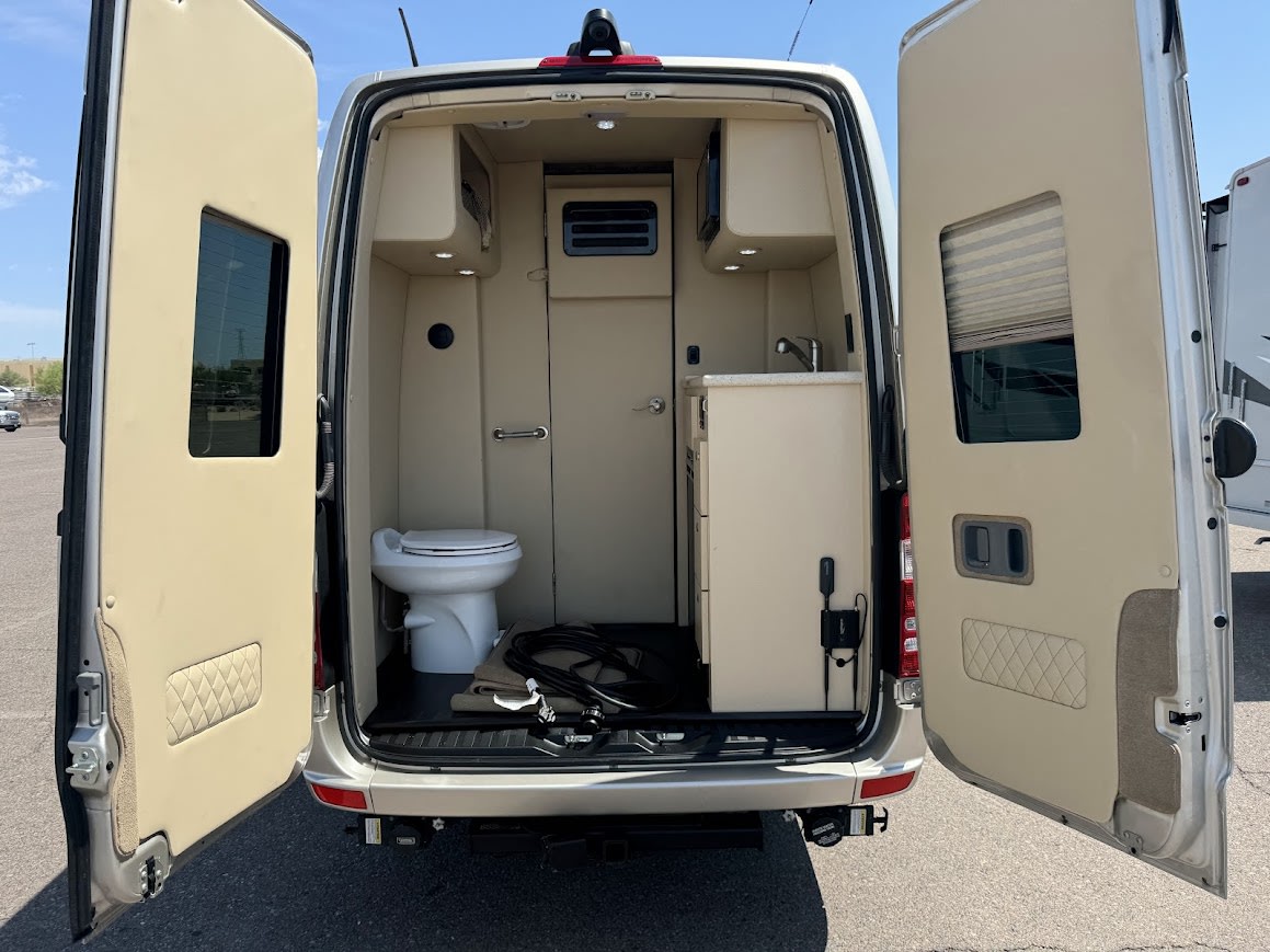 Rear view of an RV rental's open doors, showing a compact interior with toilet & kitchen. — photo 3