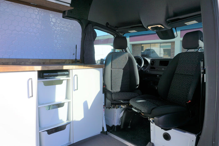 Custom rv rental: Modern campervan interior with tiled kitchen, wooden counter, storage, and front seats.