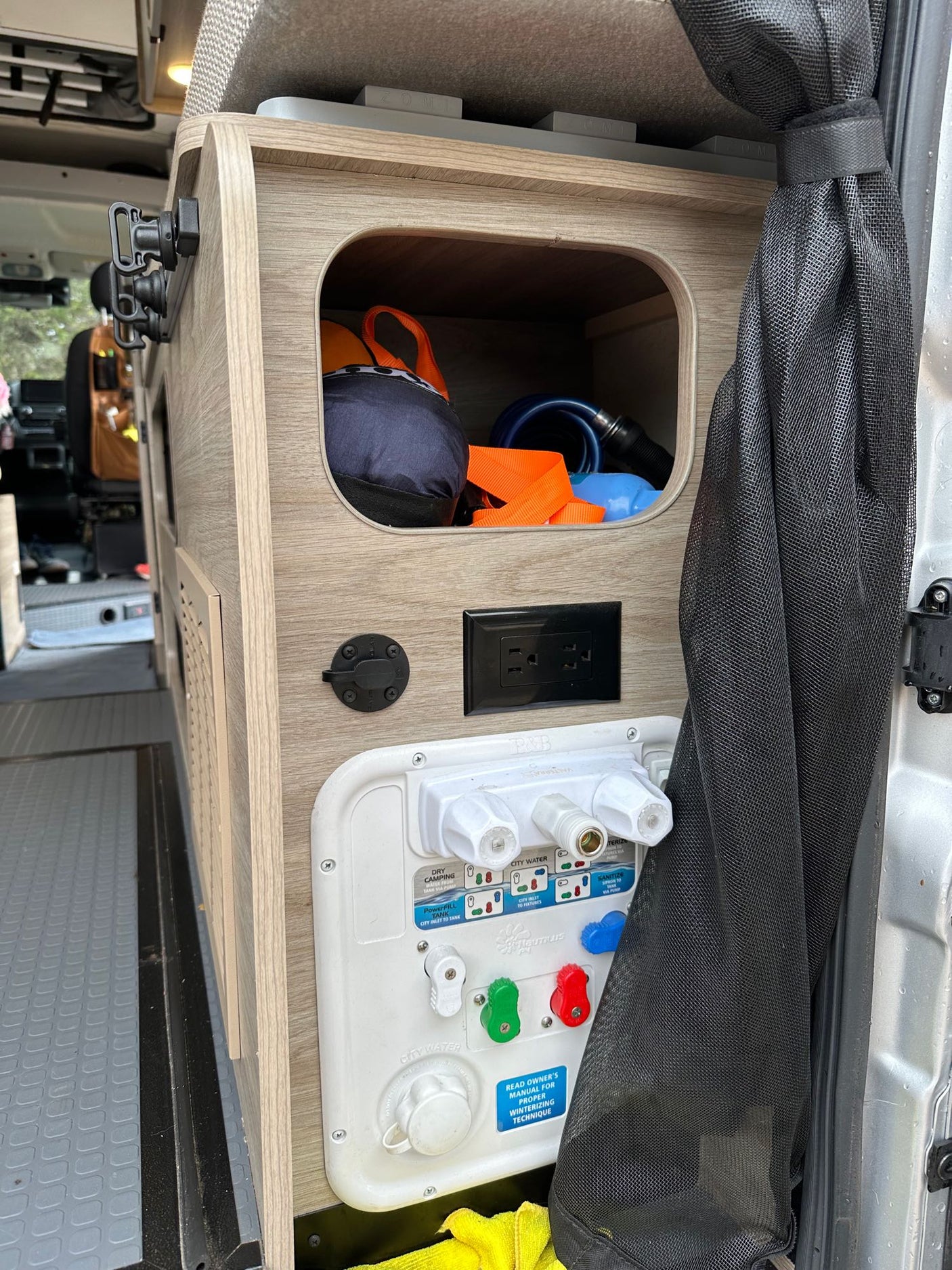 RV rental's compact interior: water utility panel with hookups, power outlet, and storage cubby.
