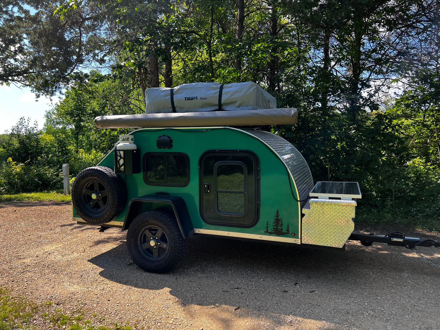 A small, green teardrop camper trailer with a rooftop tent & solar panels, ideal for an rv rental adventure.