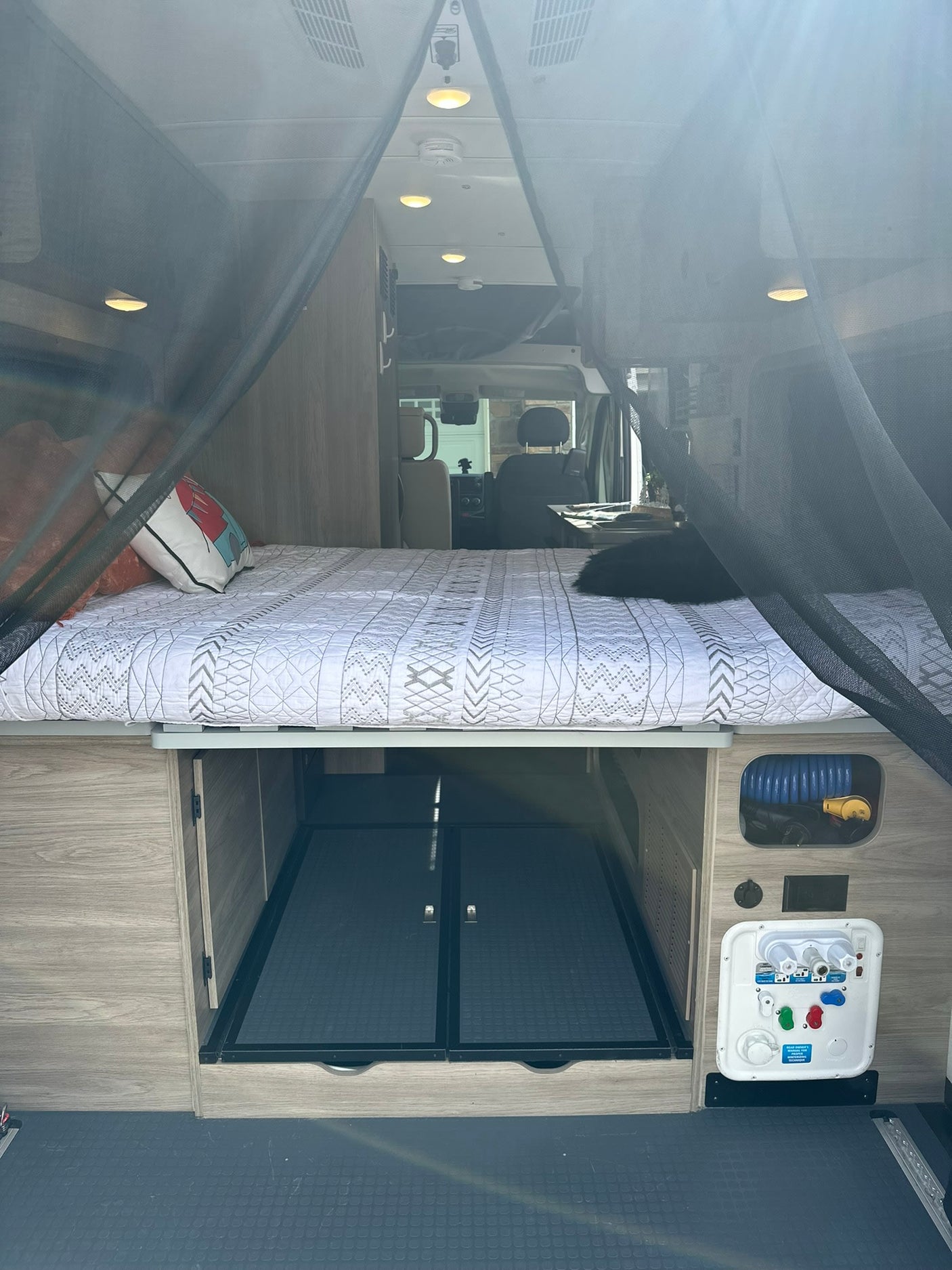 Cozy rv rental interior featuring a bed with a black pet, under-bed storage, and a water utility panel.