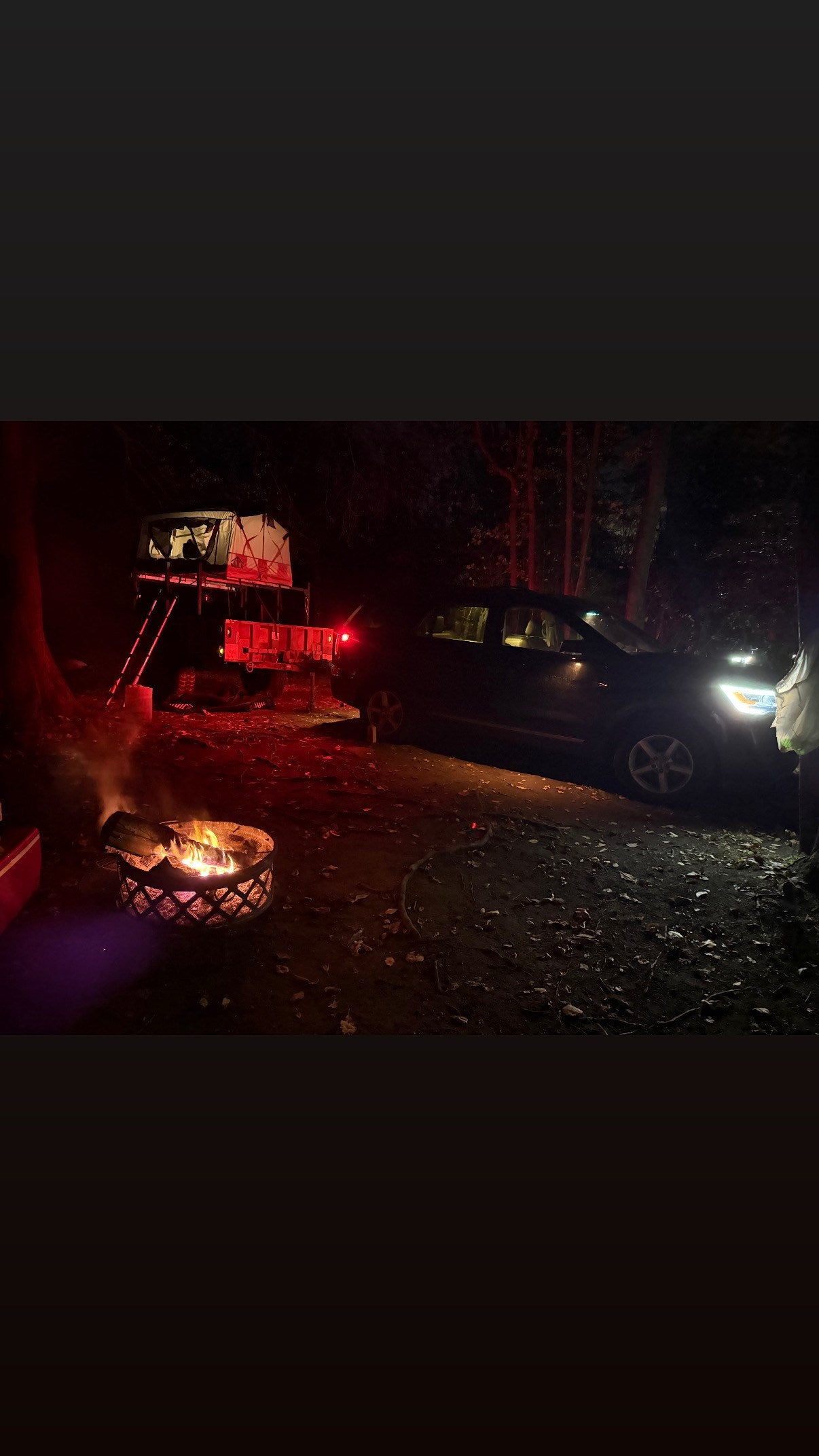Night adventure camping with an RV rental alternative: a rooftop tent on a trailer, cozy campfire, and SUV under trees.