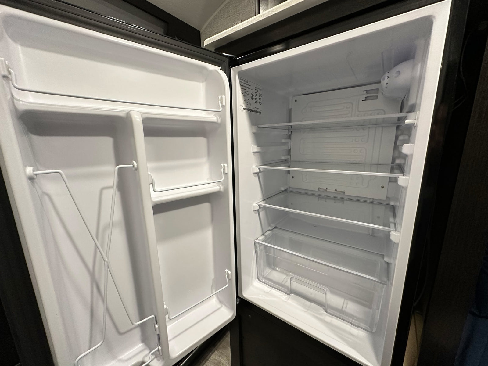 Empty RV rental refrigerator interior with clear shelves, wire door racks, and a crisper drawer, ready for your trip.