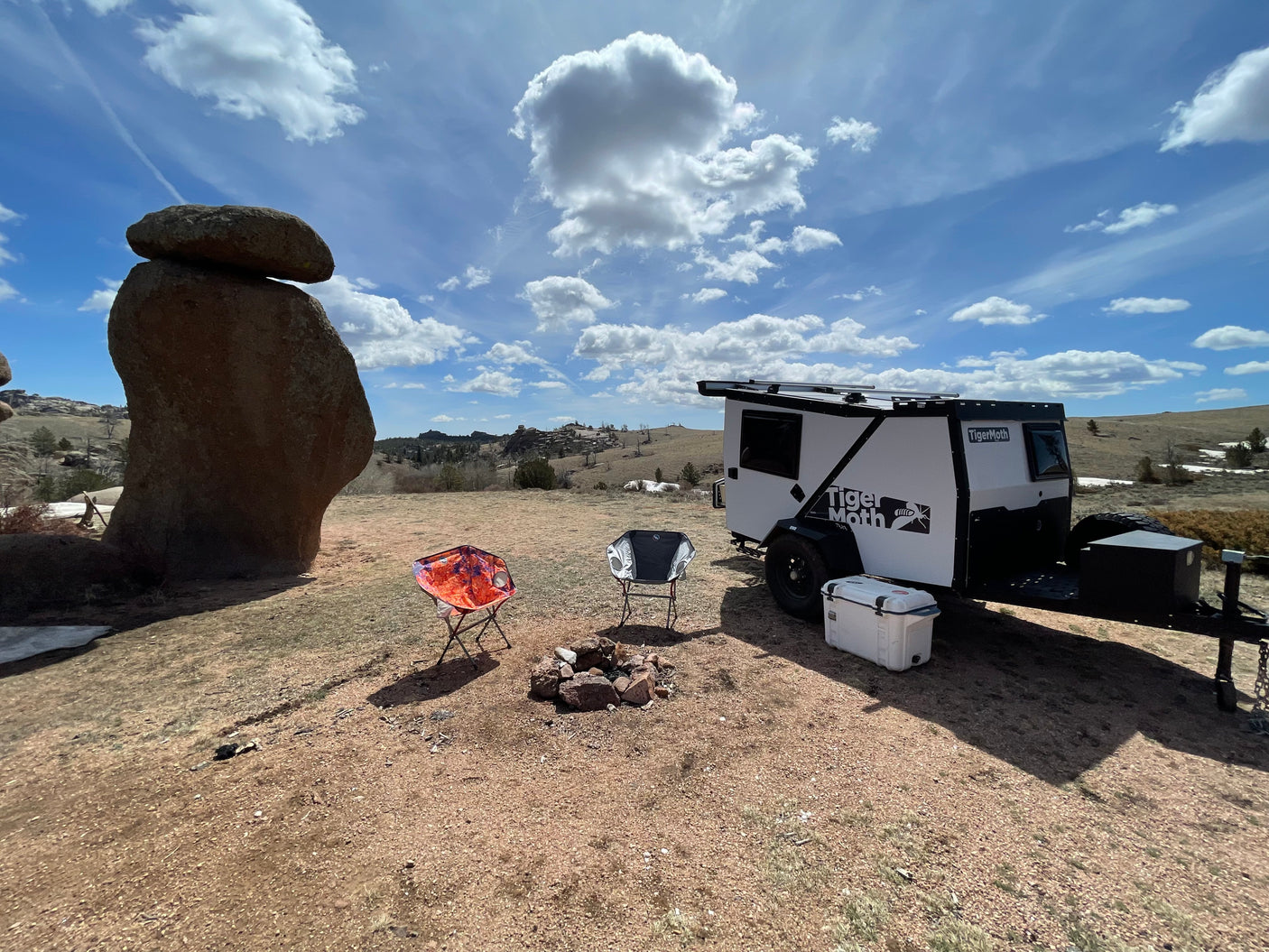 This scenic campsite features an off-road camper trailer, chairs, and fire pit, ideal for an RV rental outdoor adventure.