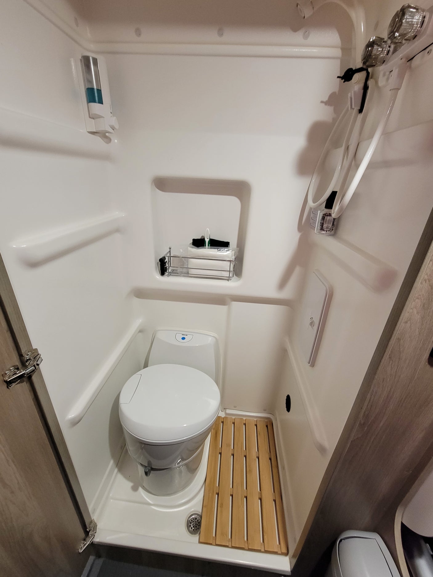 Compact RV rental wet bath with toilet, shower, soap dispenser, and wooden mat, optimized for small spaces.