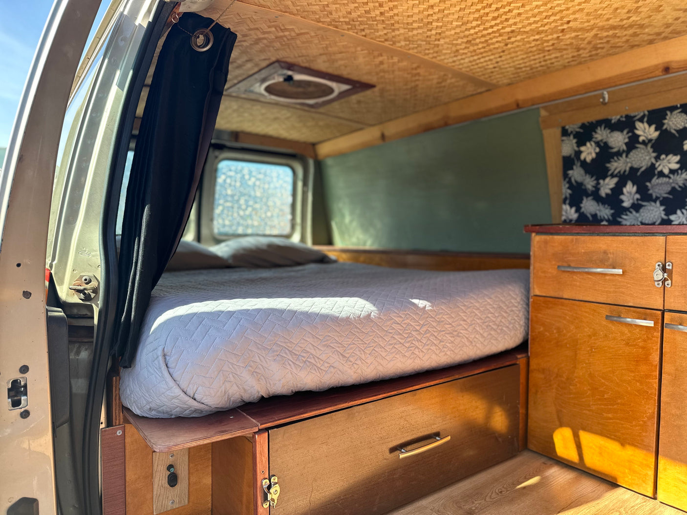 RV rental's cozy interior, showing a full bed with under-bed storage, wooden cabinetry, and a woven bamboo ceiling.