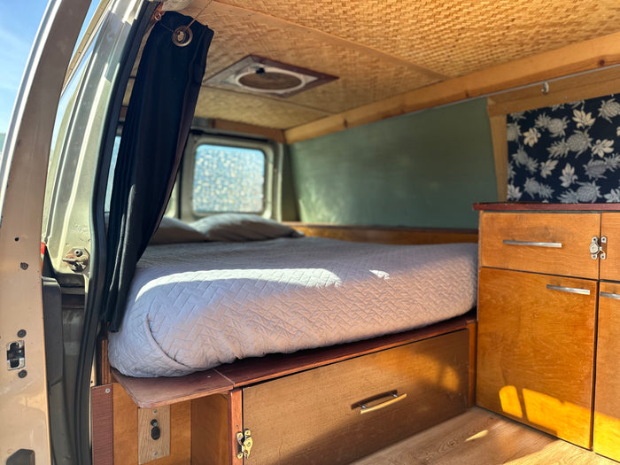 RV rental's cozy interior, showing a full bed with under-bed storage, wooden cabinetry, and a woven bamboo ceiling.