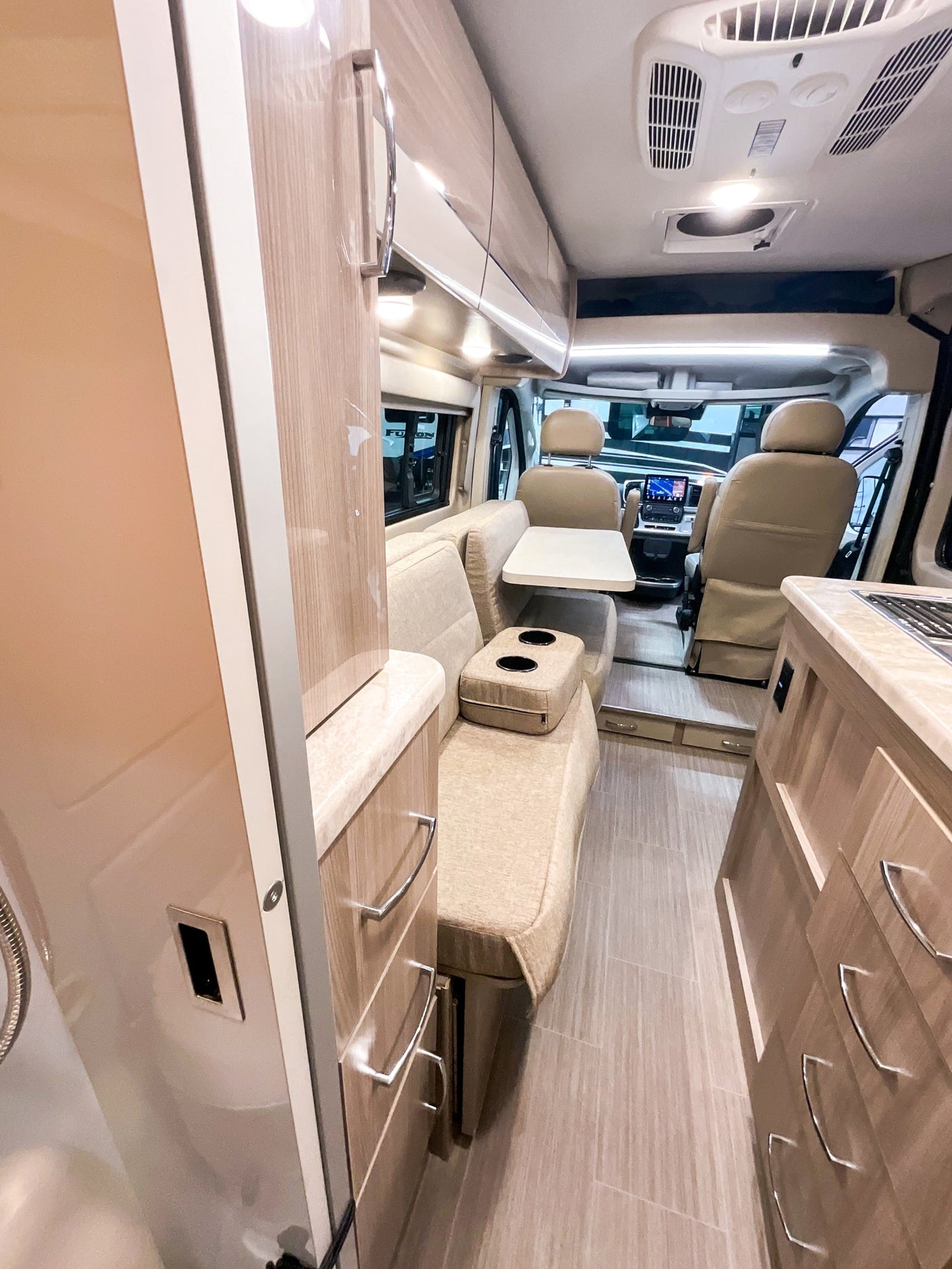 Inside a modern **rv rental**: light-toned interior with a cozy living area, dining table, kitchen counter, and front cab.