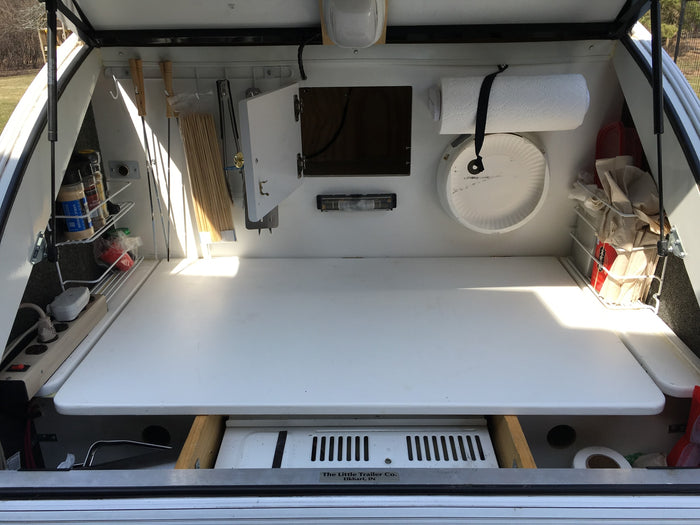 Compact RV rental outdoor kitchen in a teardrop trailer: features stove, spices, paper towels & organized storage for camping.