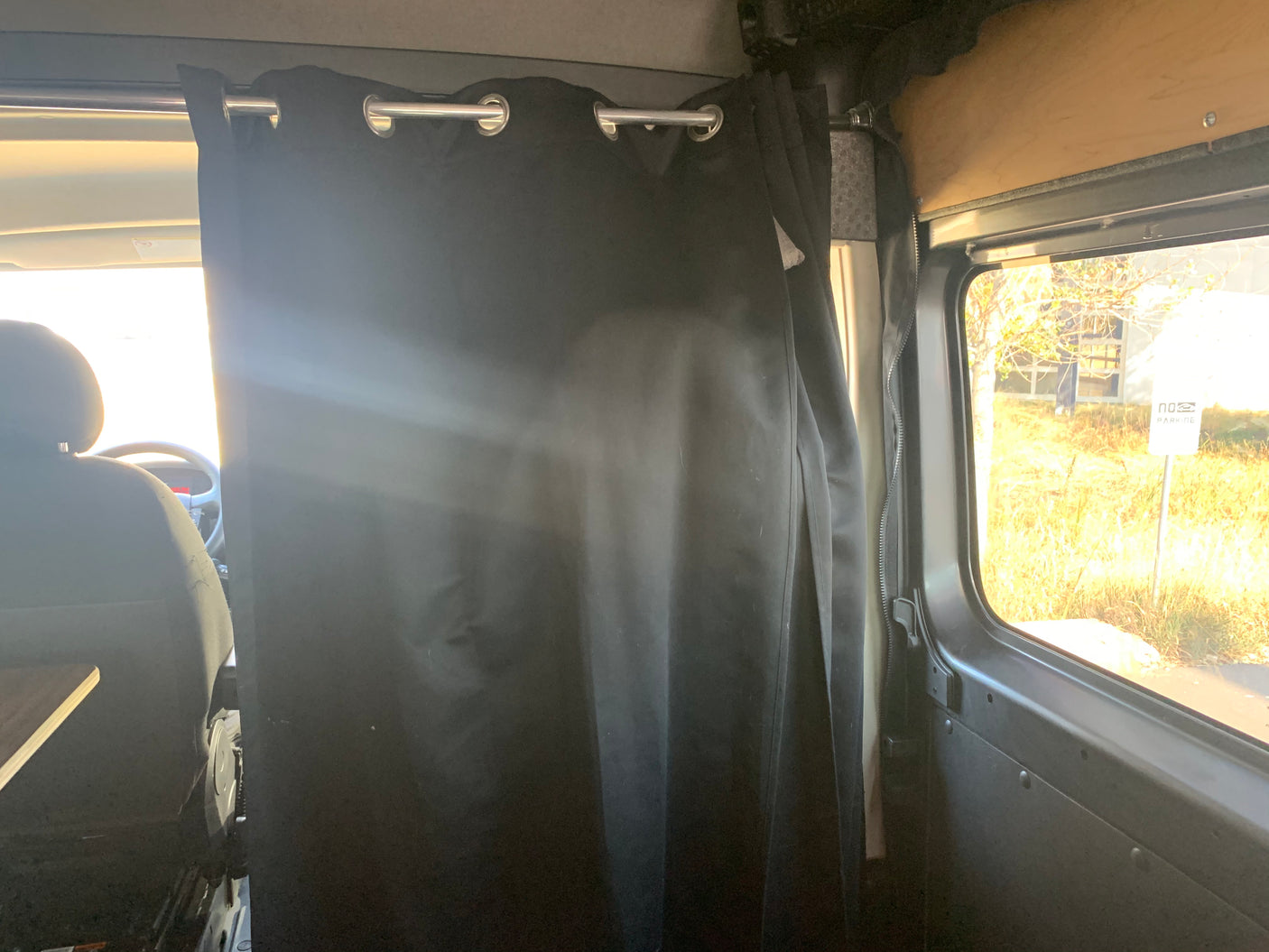 Interior of an RV rental campervan with a black privacy curtain separating the front cab from the living area, and an outdoor view.