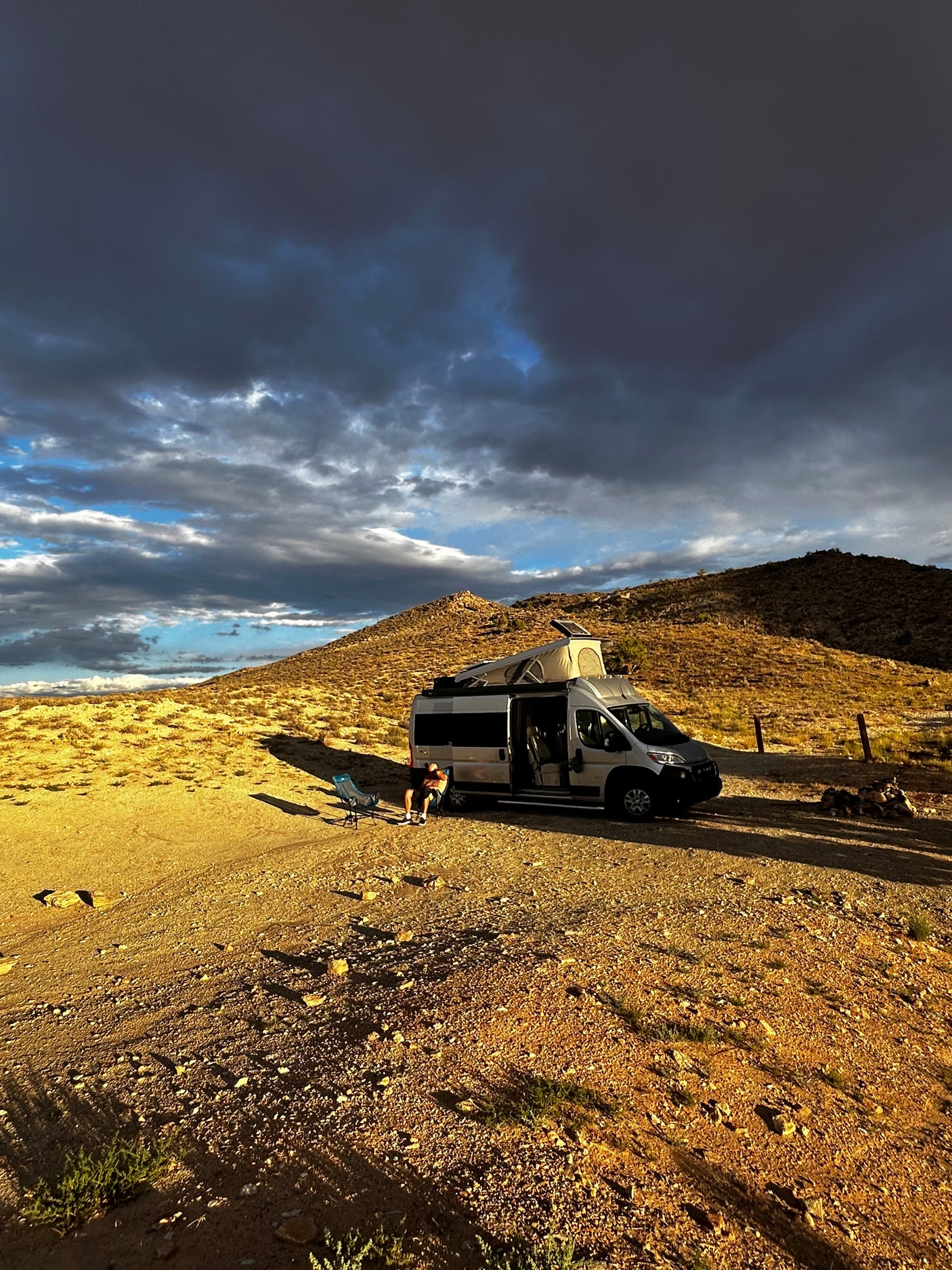RV rental parked in a serene desert landscape with a person relaxing outside, under dramatic skies.