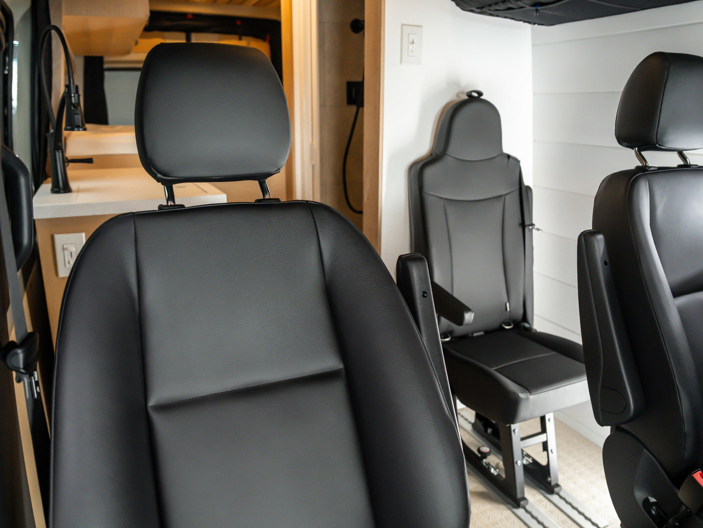 Inside an RV rental: comfortable black passenger seats and a glimpse of the kitchen area. Perfect for mobile living.