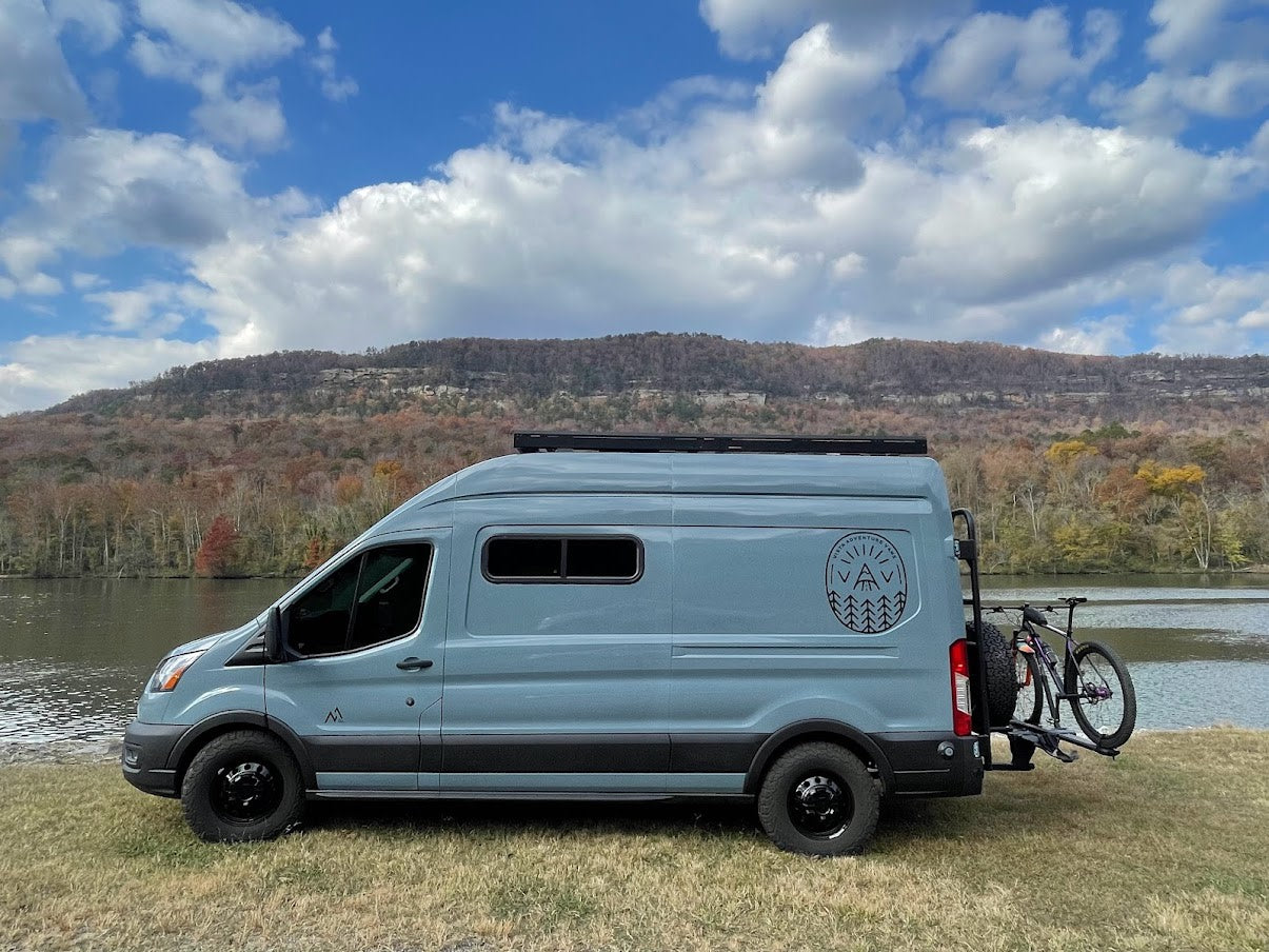 Light blue adventure RV rental van by a lake with mountains and a bike