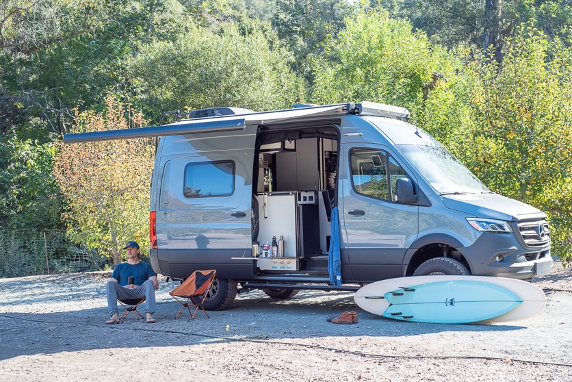 RV rental camper van, awning out, man relaxing on dirt next to surfboards. Ideal for outdoor adventures. — photo 1