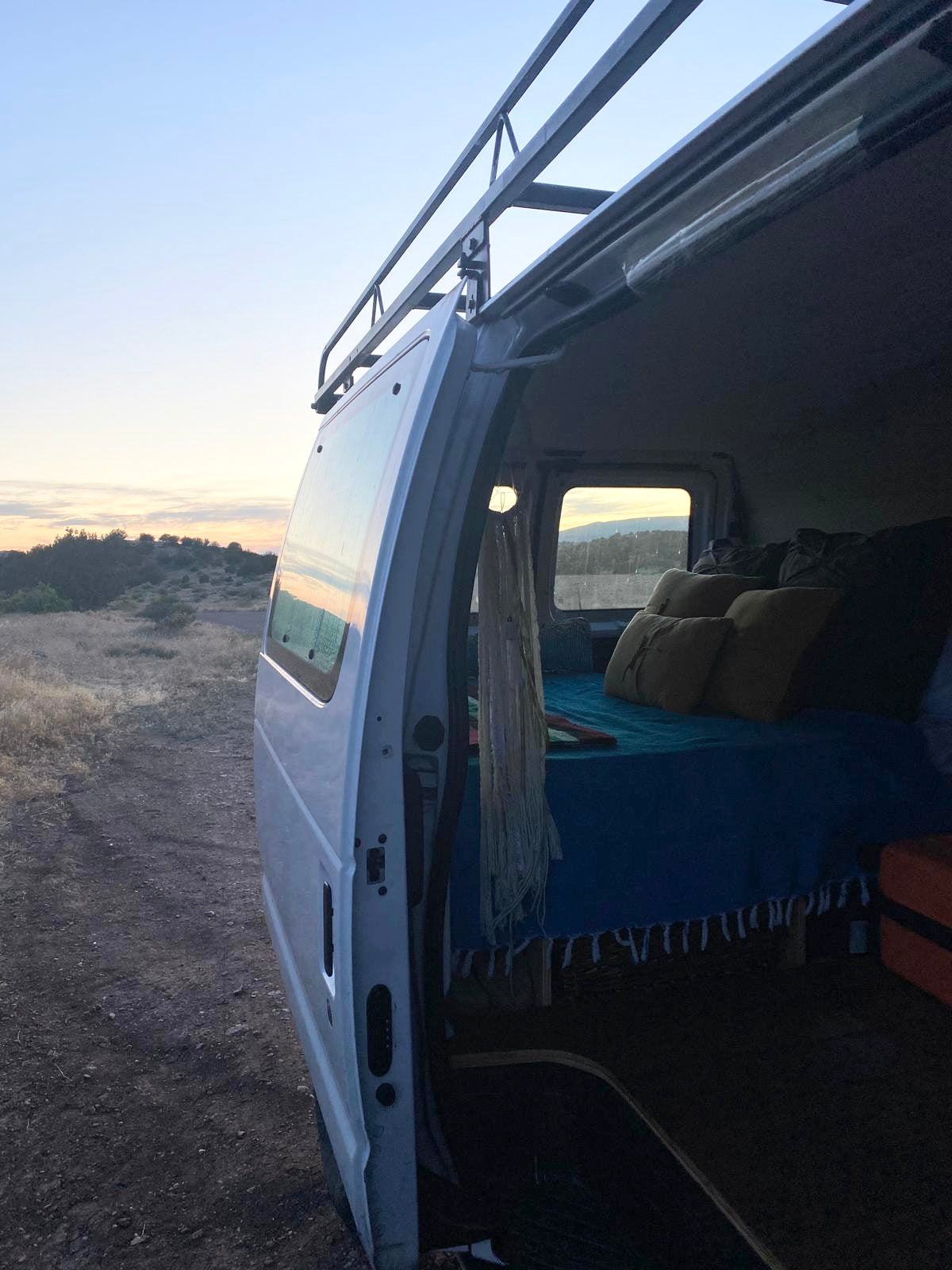 This RV rental campervan with an open door reveals a cozy bed & scenic nature views. Perfect for adventure travel.