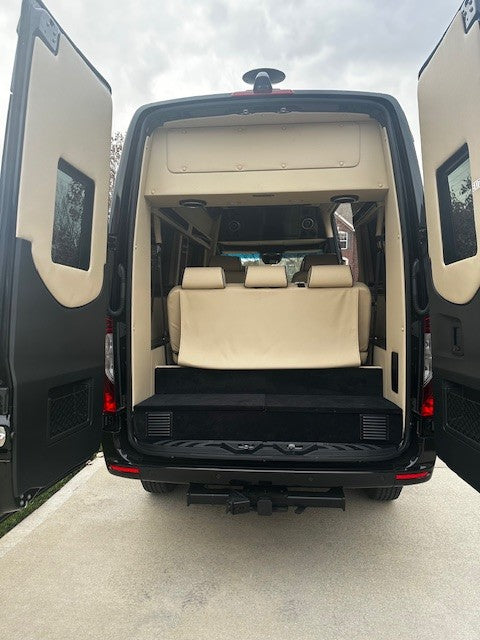 Open rear doors of a black luxury Sprinter van, ready for your RV rental. Features spacious cream interior and comfortable seating.