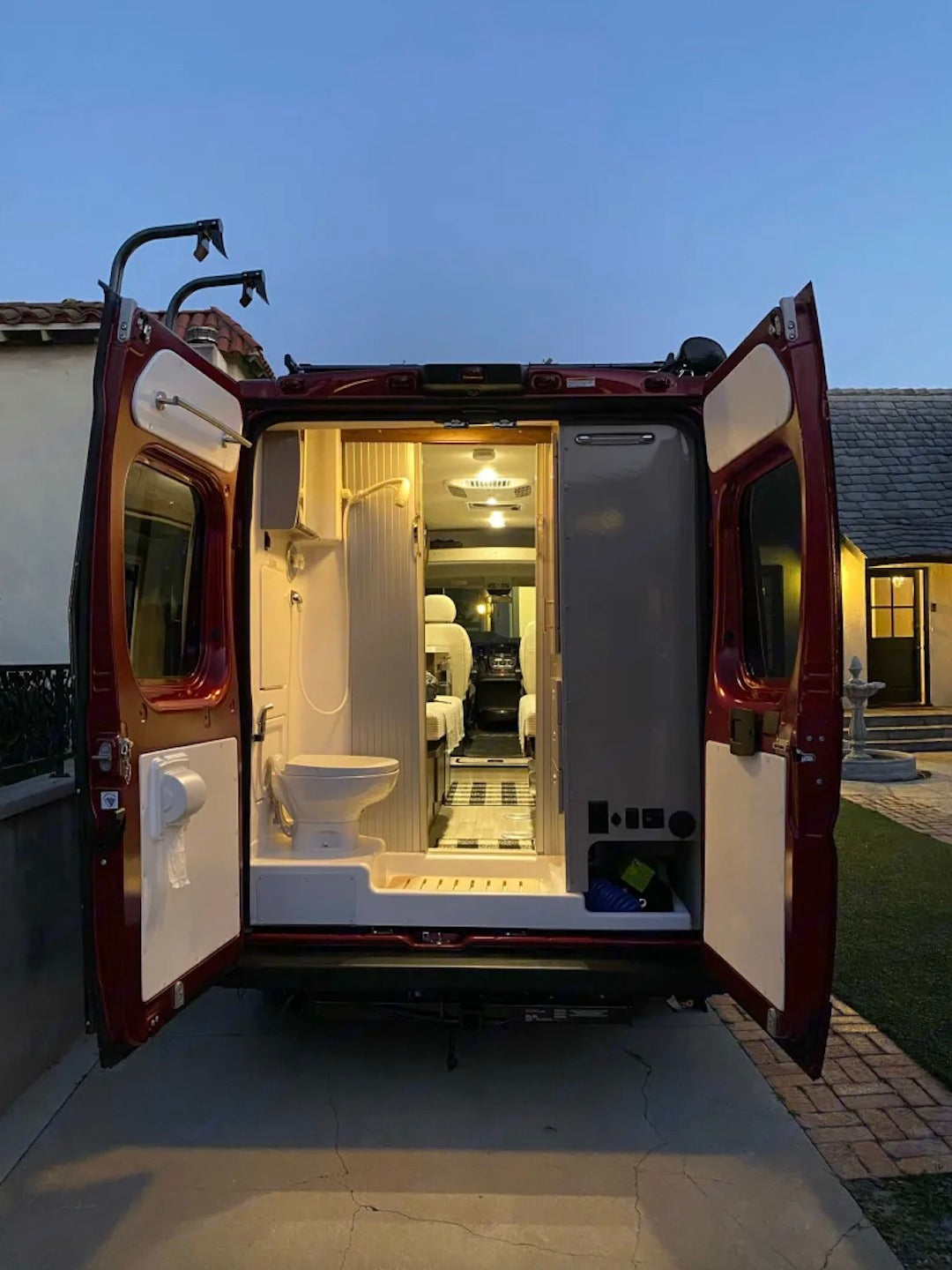 Rear view of an RV rental's interior: a compact camper van with a full bathroom (toilet, shower) and living area.