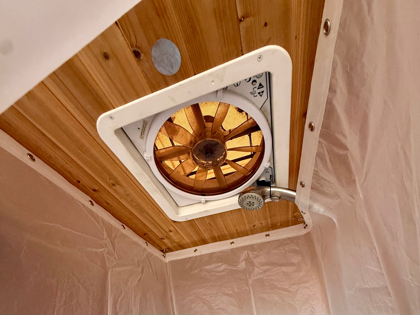 This RV rental wet bath features a wood-paneled ceiling, vent fan, shower head, and a light shower curtain.