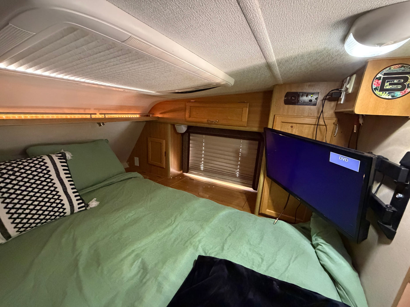 Cozy RV rental bedroom featuring a green bed, mounted TV, wooden accents, and overhead lighting for a comfortable stay.