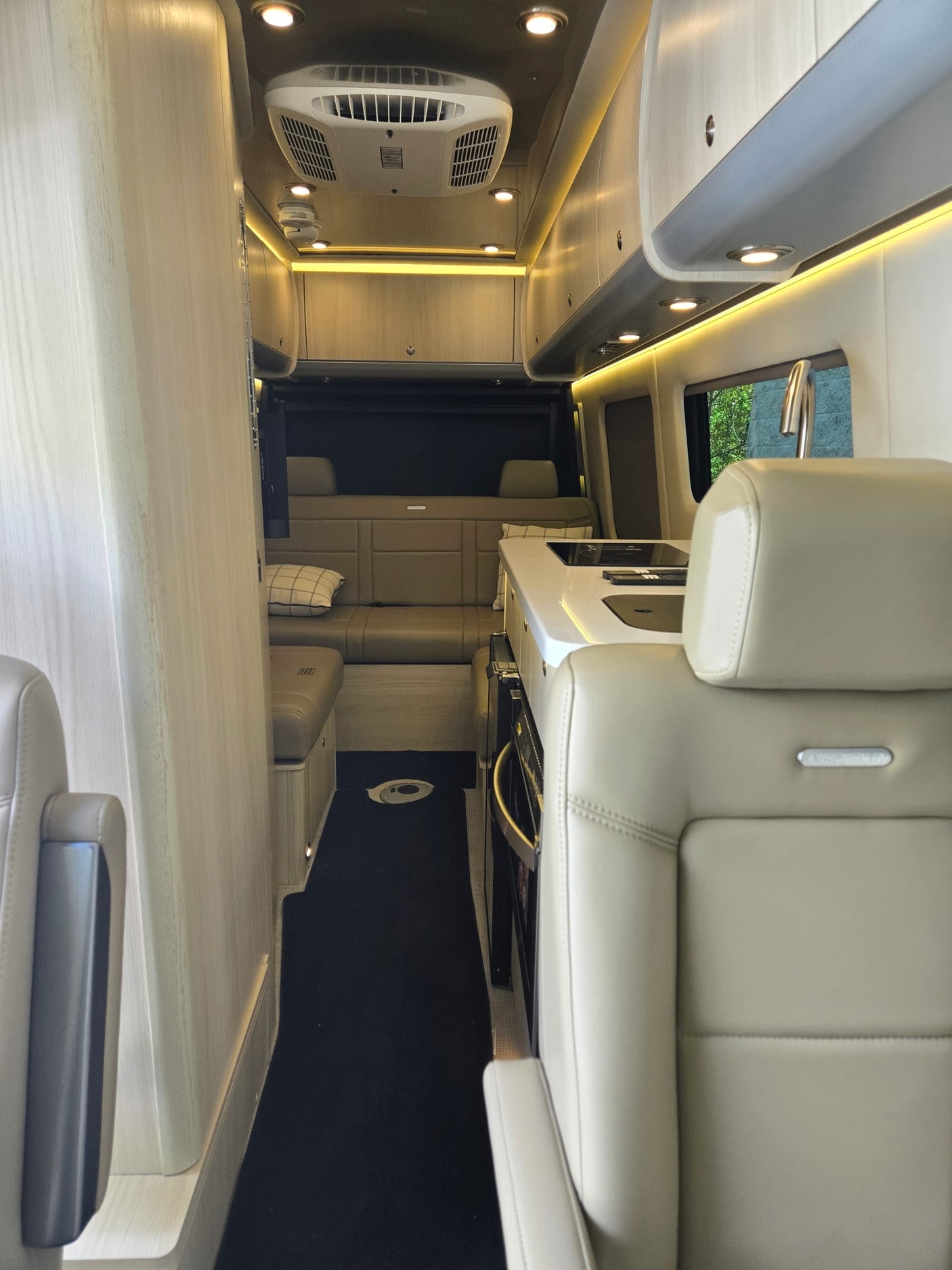 Modern rv rental interior: light wood and tan upholstery, full kitchen, bright lighting, and rear lounge/bed area for adventures.
