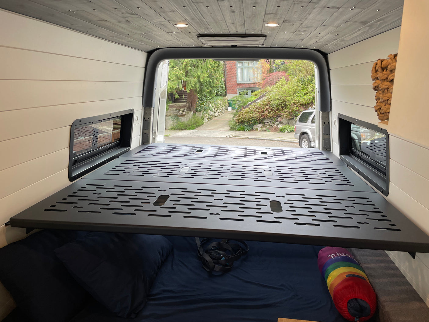 Spacious RV rental van interior with a modular bed platform over cozy bedding, light paneling, and a wood ceiling.
