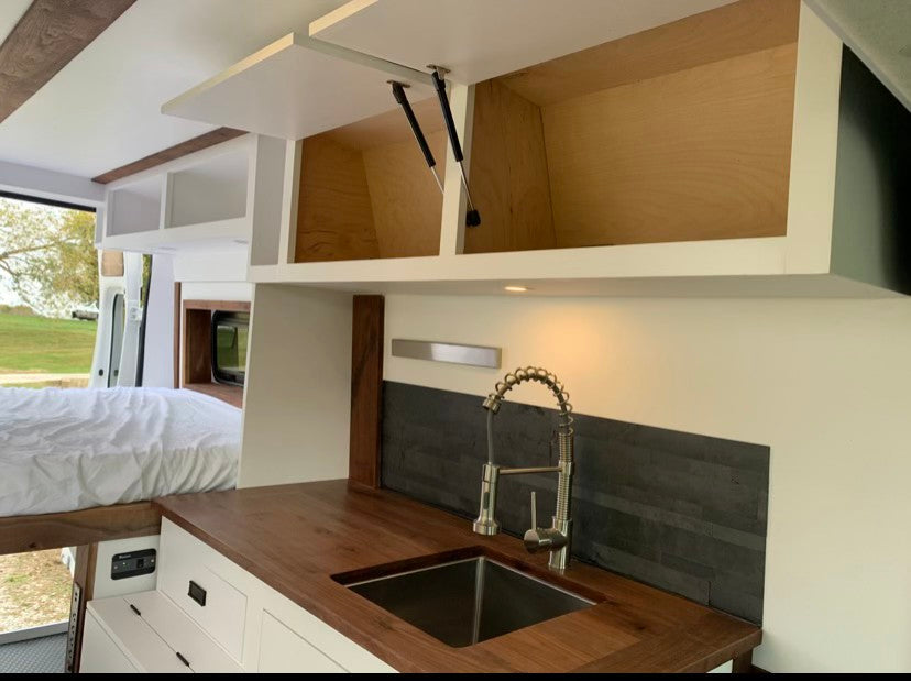 Modern RV rental interior: custom kitchen with sink, overhead storage, & a comfy bed. Your adventure awaits!