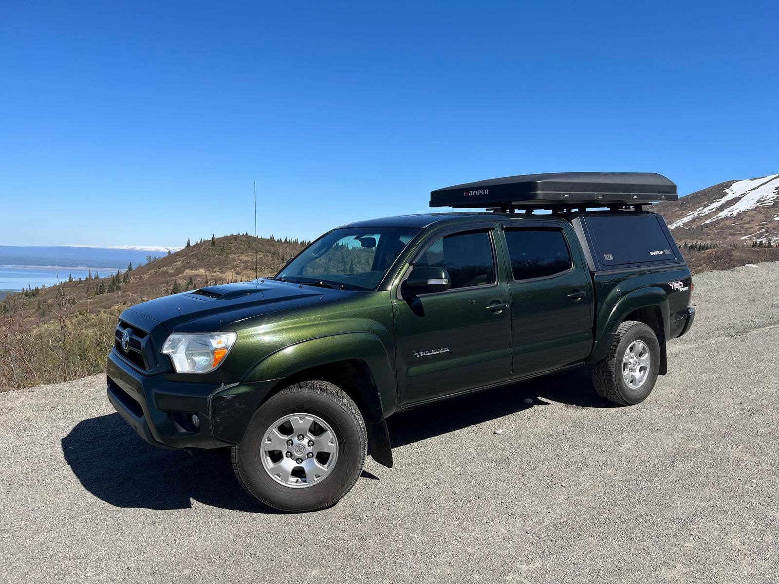 This green Toyota Tacoma, equipped with an iKamper tent & SmartCap, offers a unique adventure, akin to an RV rental in the mountains.