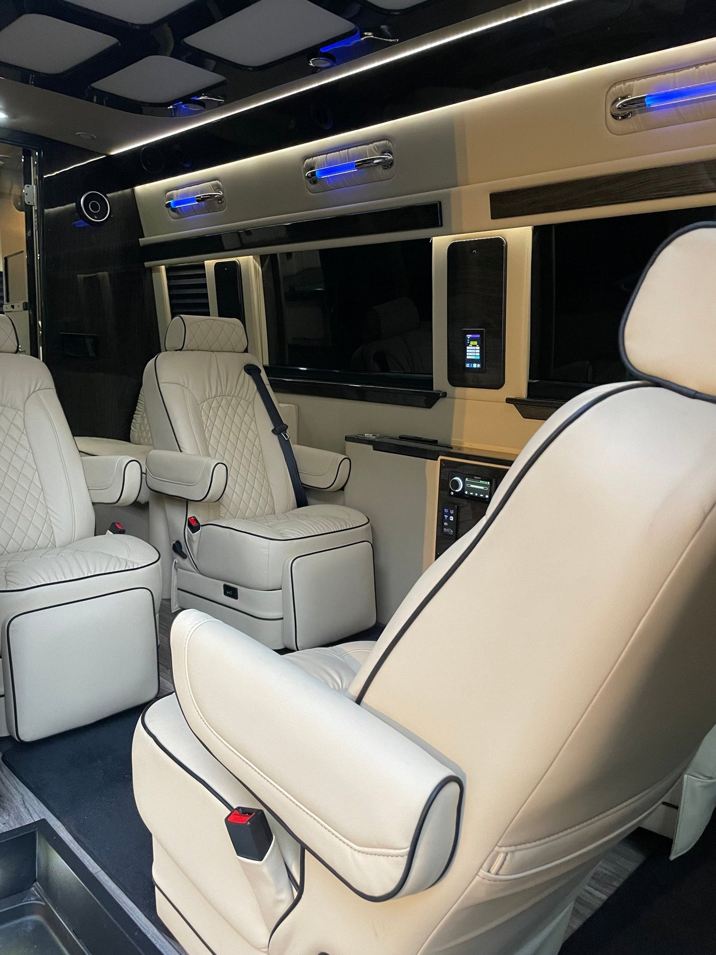 Plush cream leather interior of a luxury RV rental, featuring captain's chairs, ambient blue lighting, and infotainment controls.