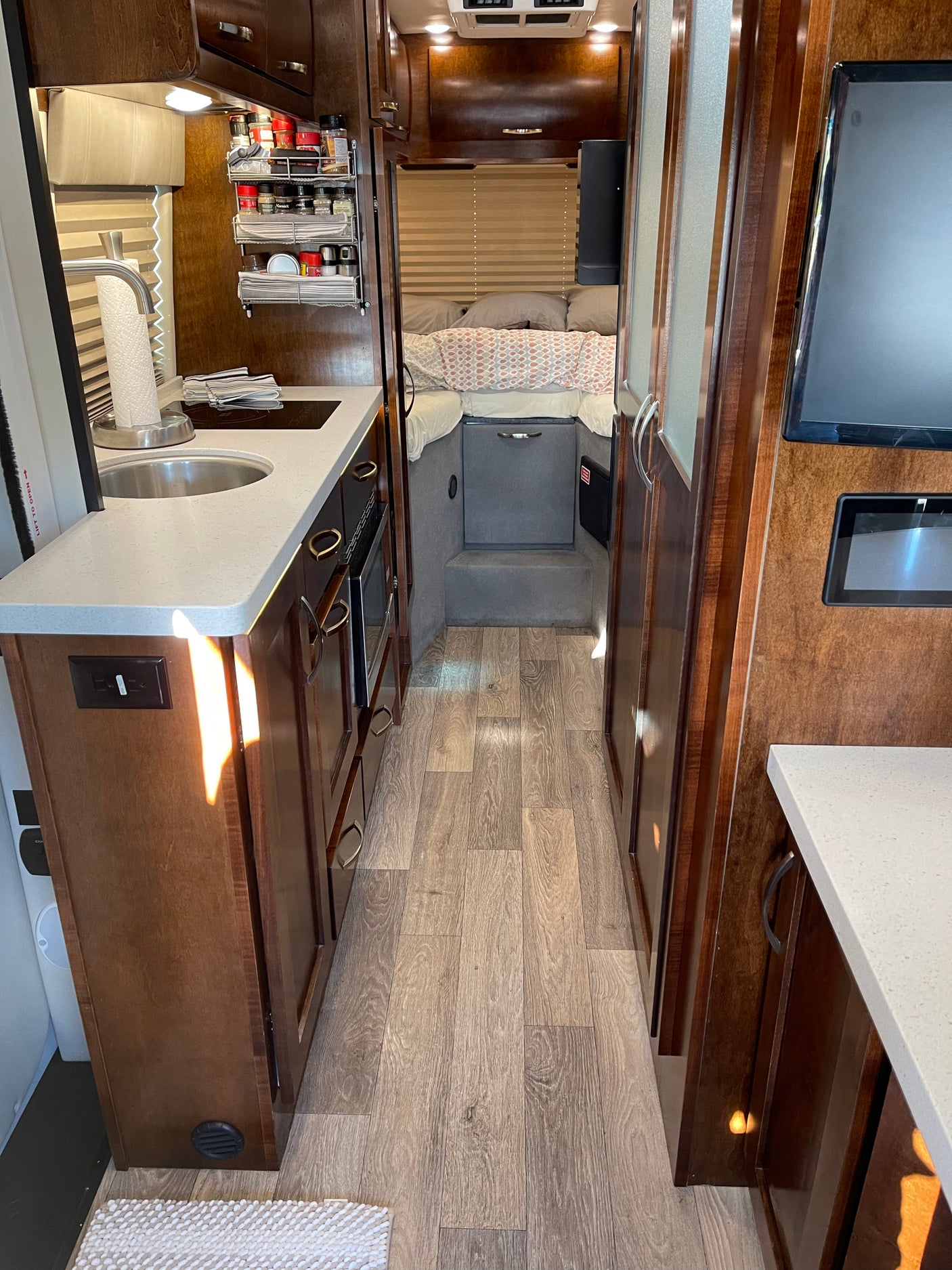 This RV rental interior showcases a compact kitchen, cozy sleeping area, and wood-look floors, perfect for mobile adventures.