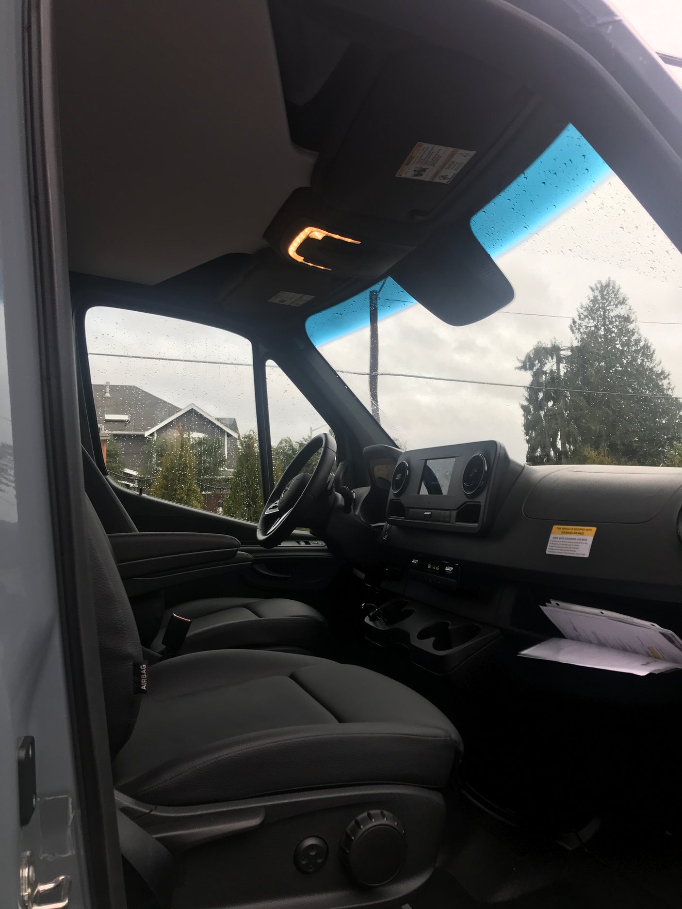 Interior of an RV rental van: driver's seat, dashboard, and a rainy view through the windshield.