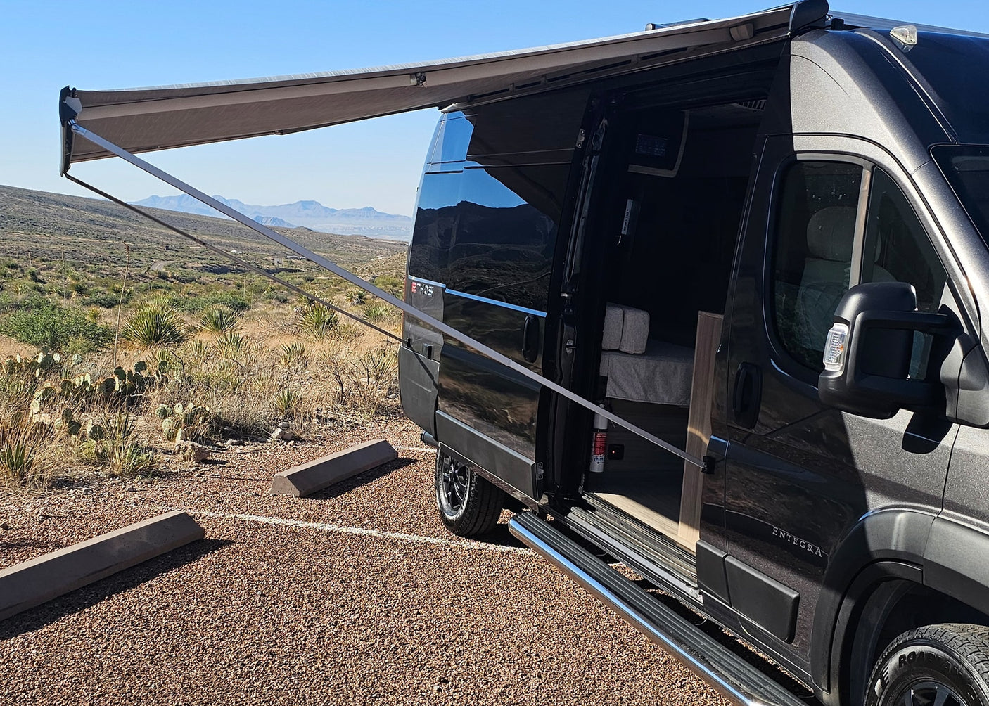 parked in gravel with desert mountains in the background.|Dark grey camper van RV rental parked on a gravel road