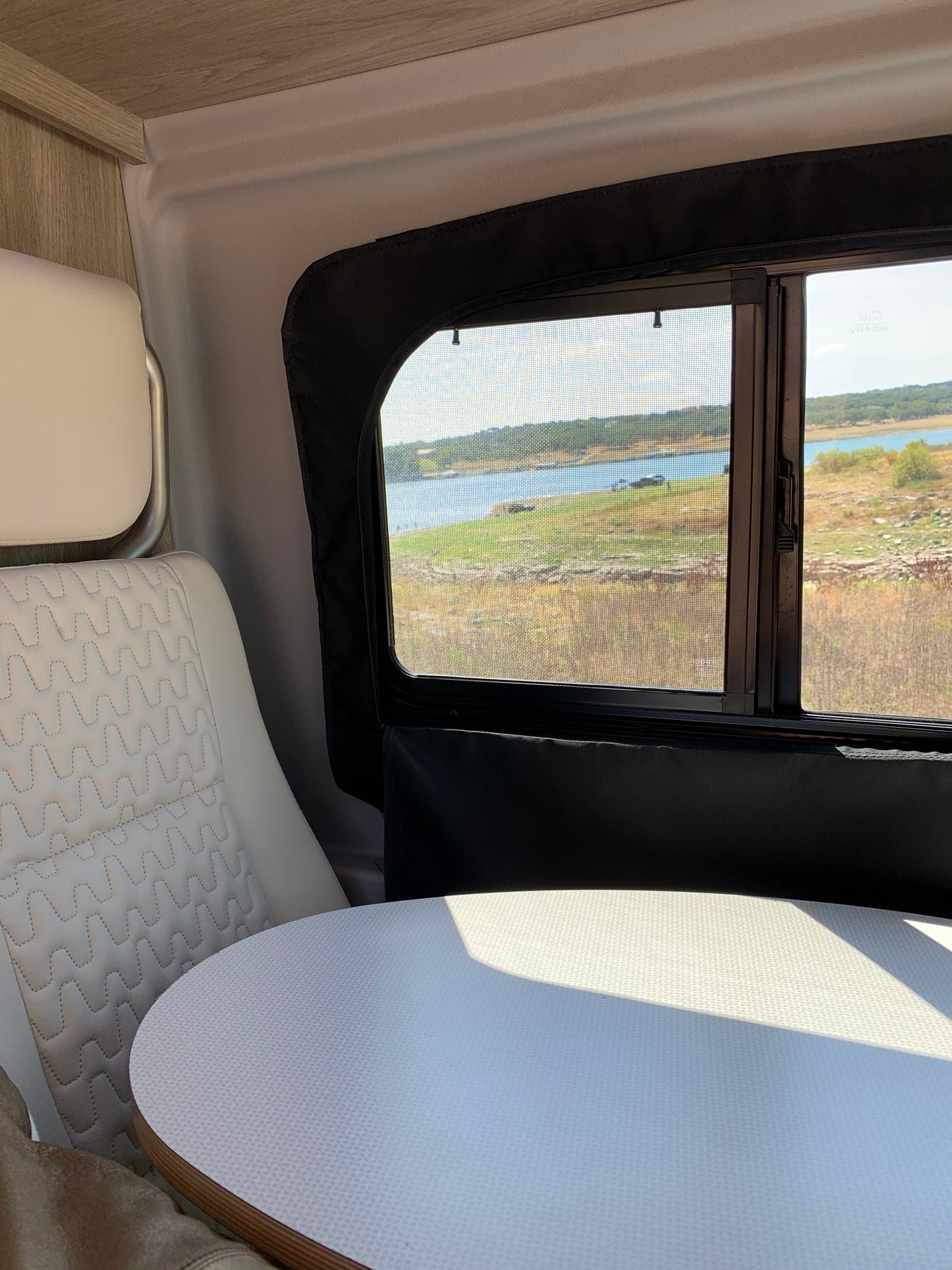 Relaxing in an RV rental, featuring a round table, comfy quilted seat, and a screened window showcasing a lake view.
