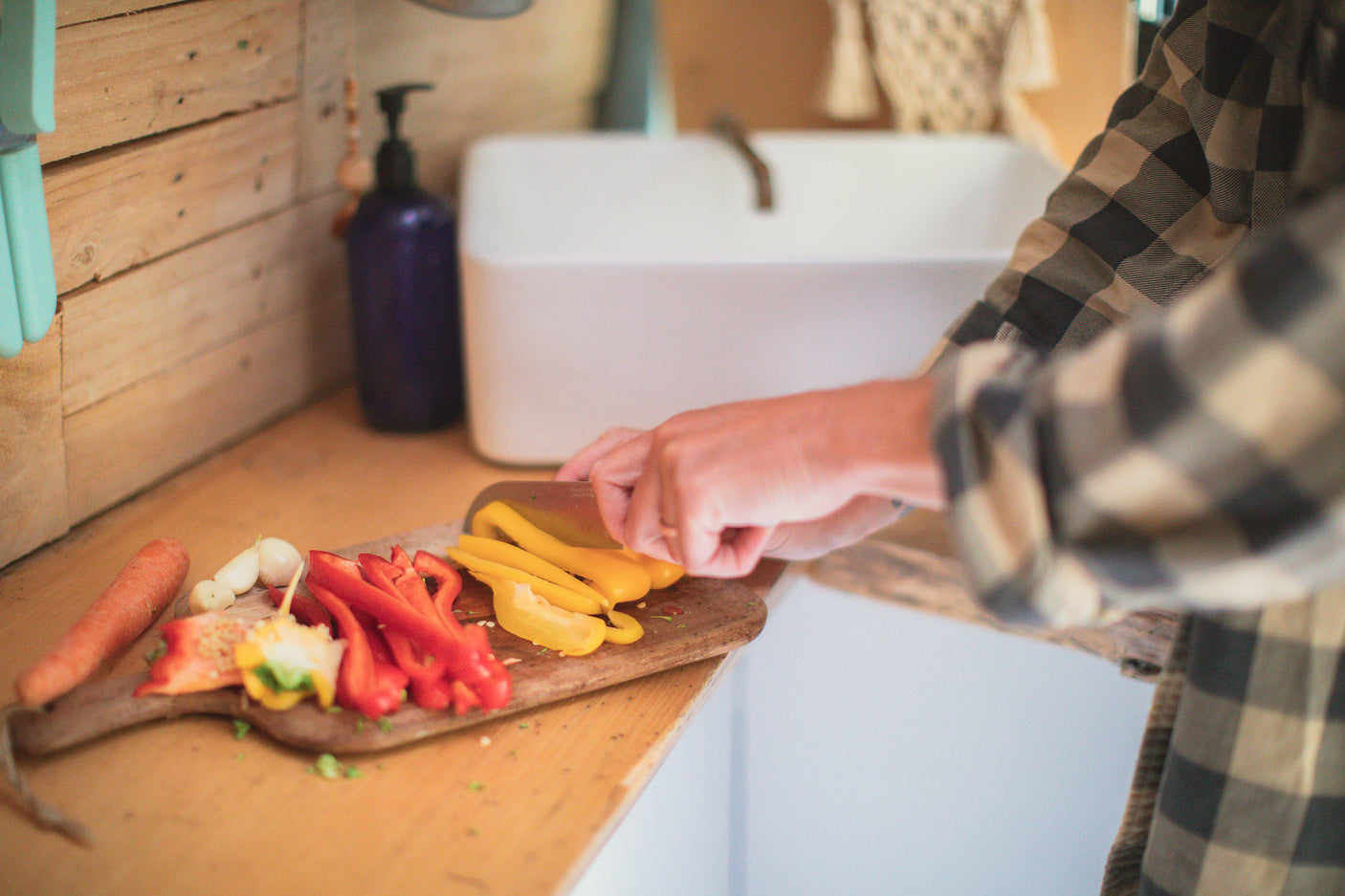 A person chops bell peppers and garlic on a wooden board in a cozy RV rental kitchen.