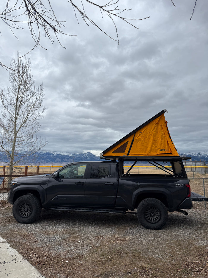 Dark grey Toyota Tacoma overland truck with orange rooftop tent. Great for camping, an alternative to an RV rental adventure.