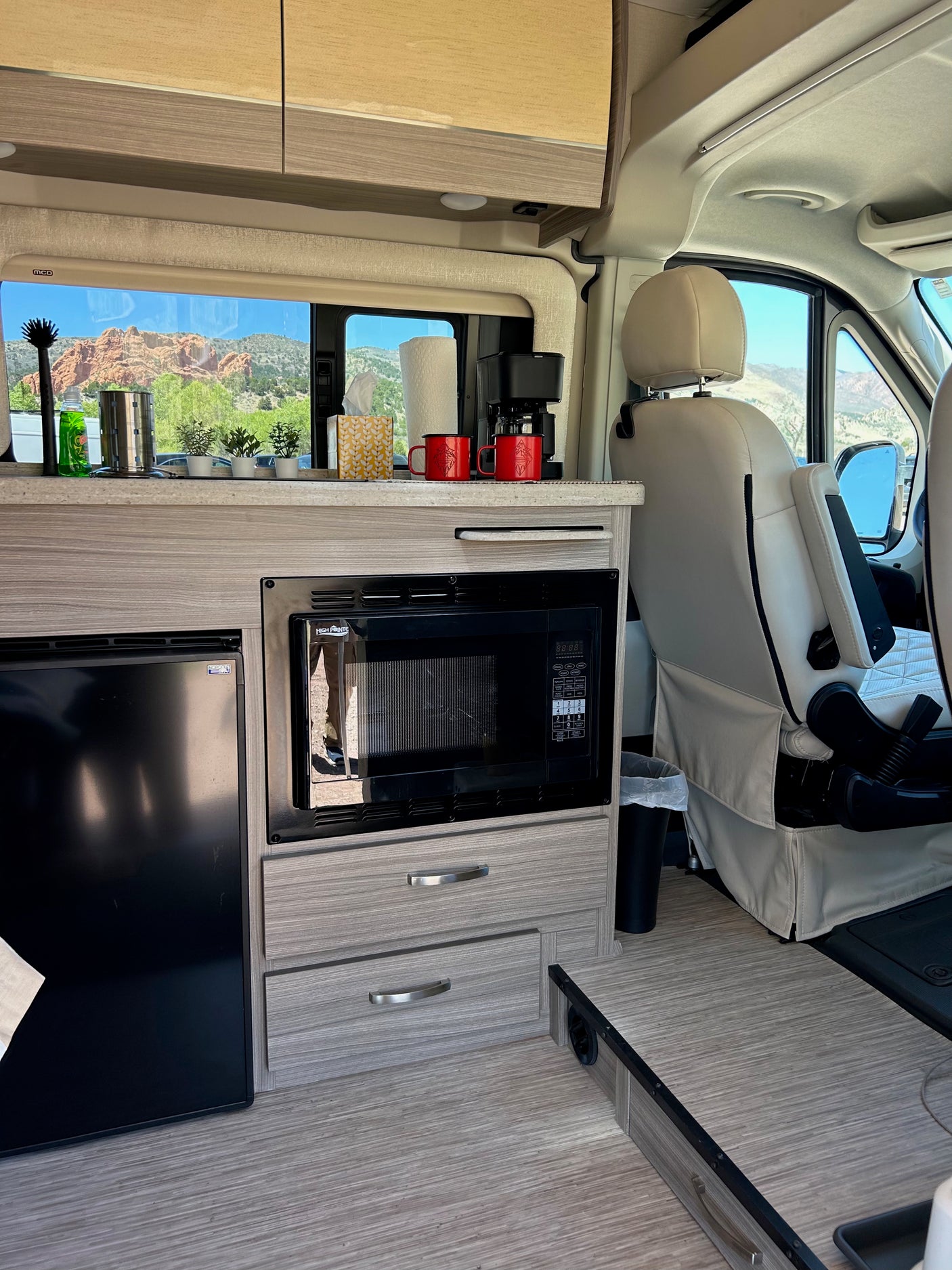 This RV rental kitchen features a microwave, fridge, coffee maker, and a scenic mountain view from the window.